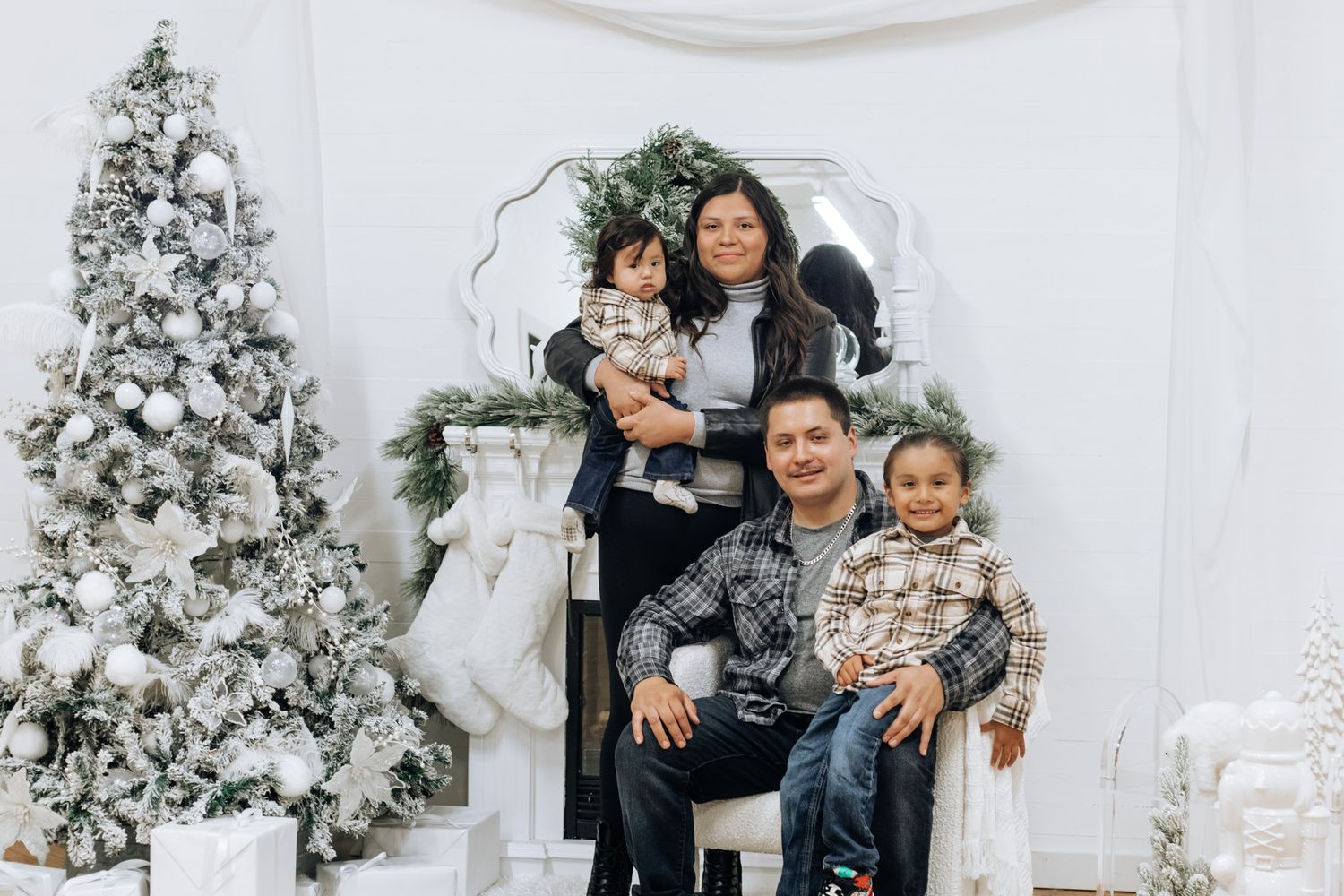 Family posing together in front of decorated white Christmas trees and fireplace during holiday photo session.