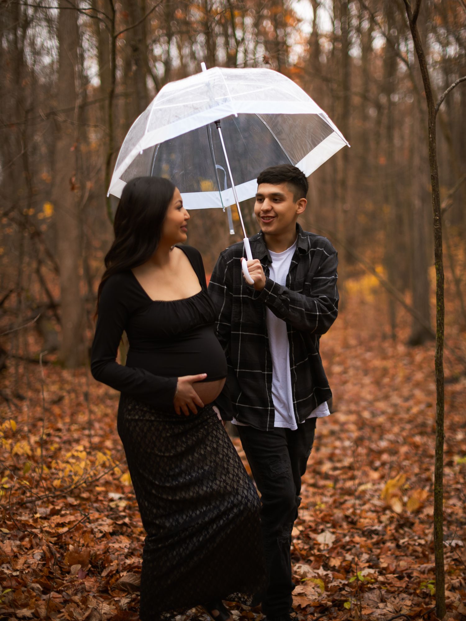 A couple sharing a moment under a clear umbrella in an autumn forest.