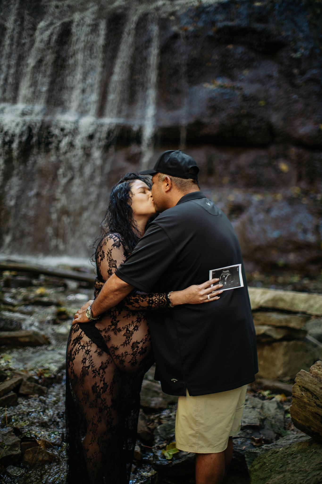 Romantic waterfall photoshoot featuring a couple in an intimate embrace against rocky cliffs.