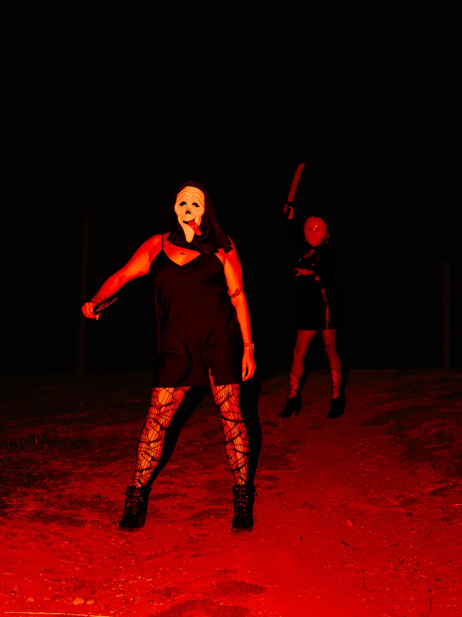 Red-tinted photo of masked figures in dramatic poses against dark background.