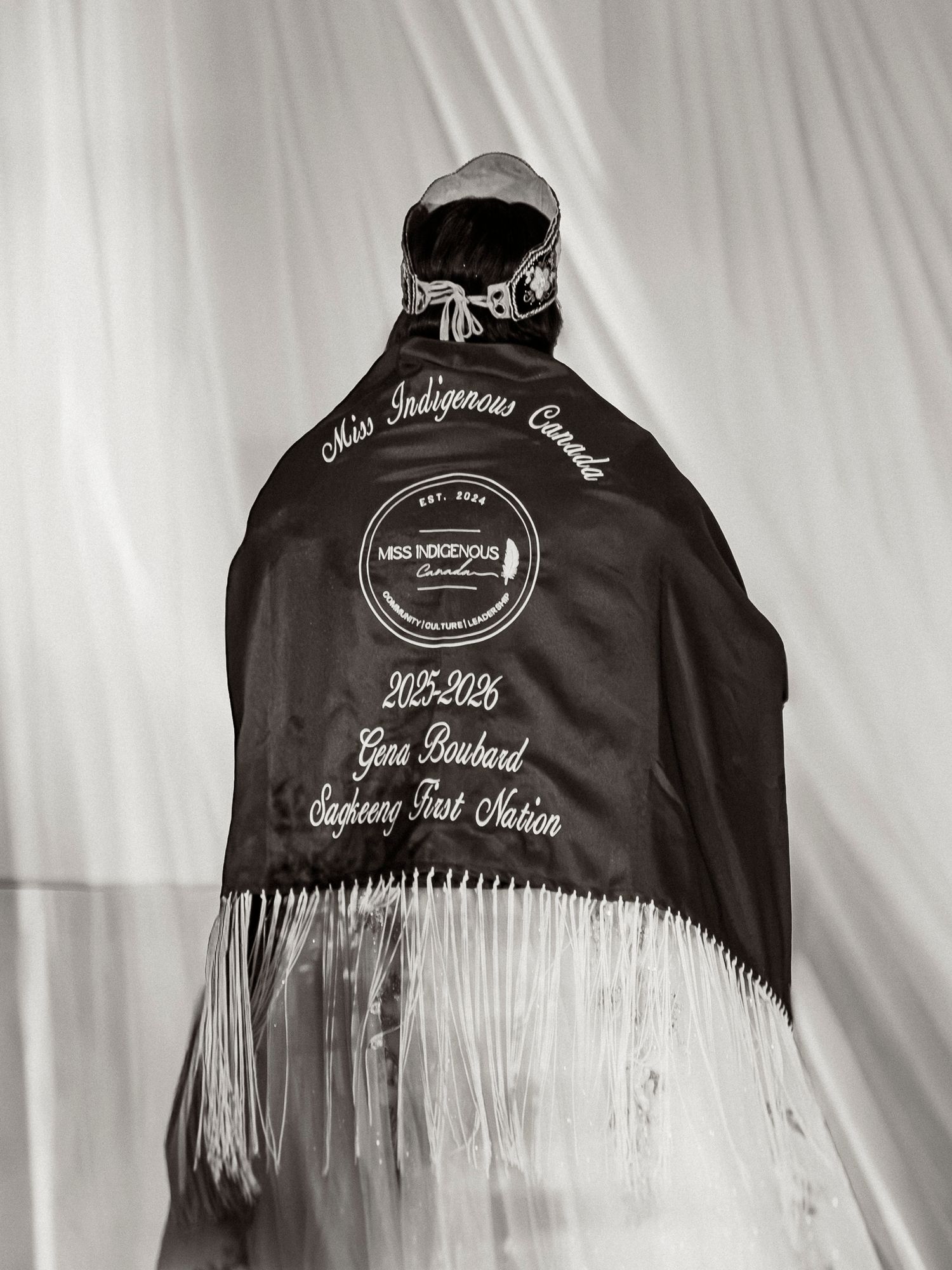 Black satin cape for Miss Indigenous Canada 2025-2026, Gera Boubard, Sadgeens First Nation, with white fringe trim.