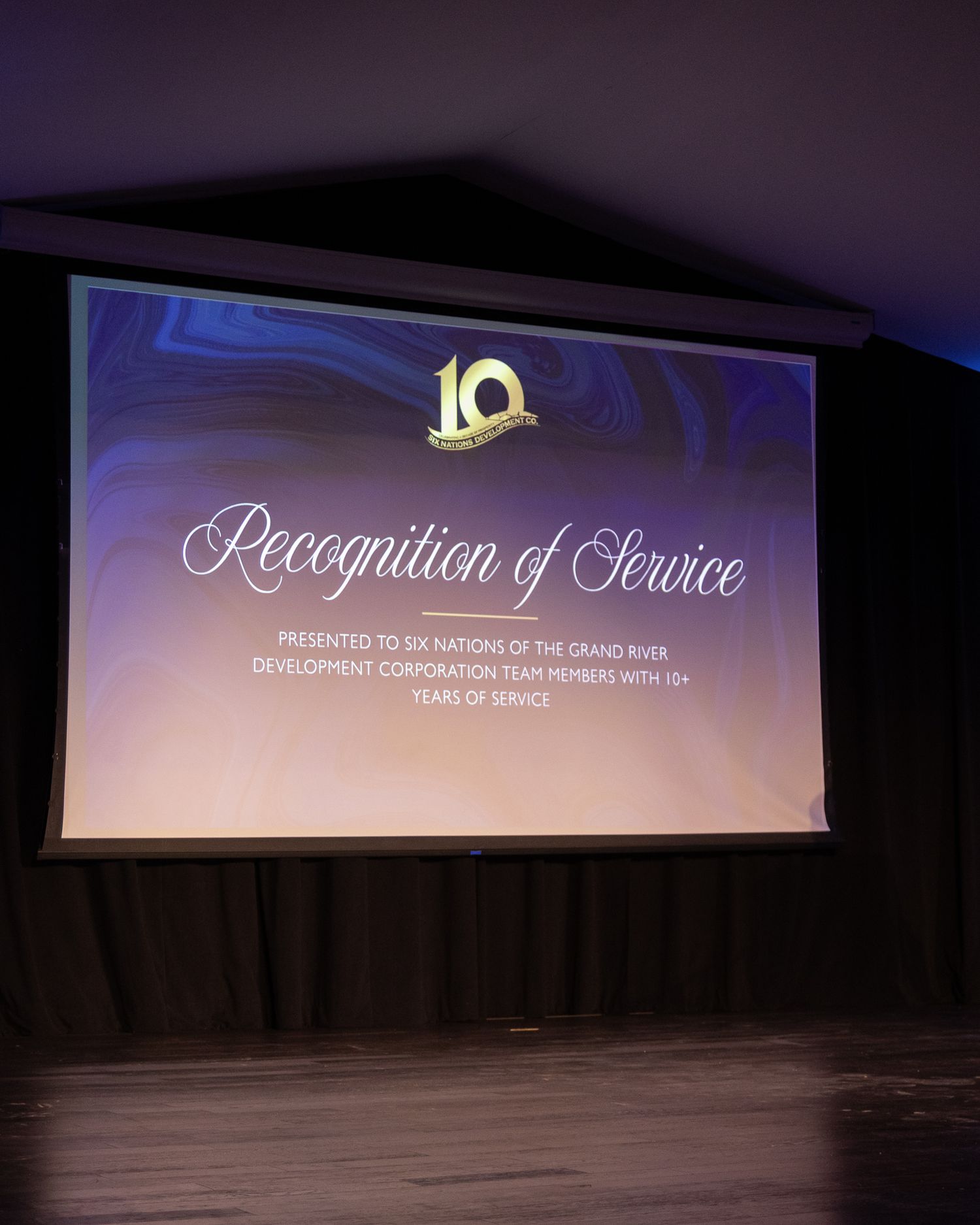 A projected screen displays a Recognition of Service award presentation for Six Nations of the Grand River Development Corporation.
