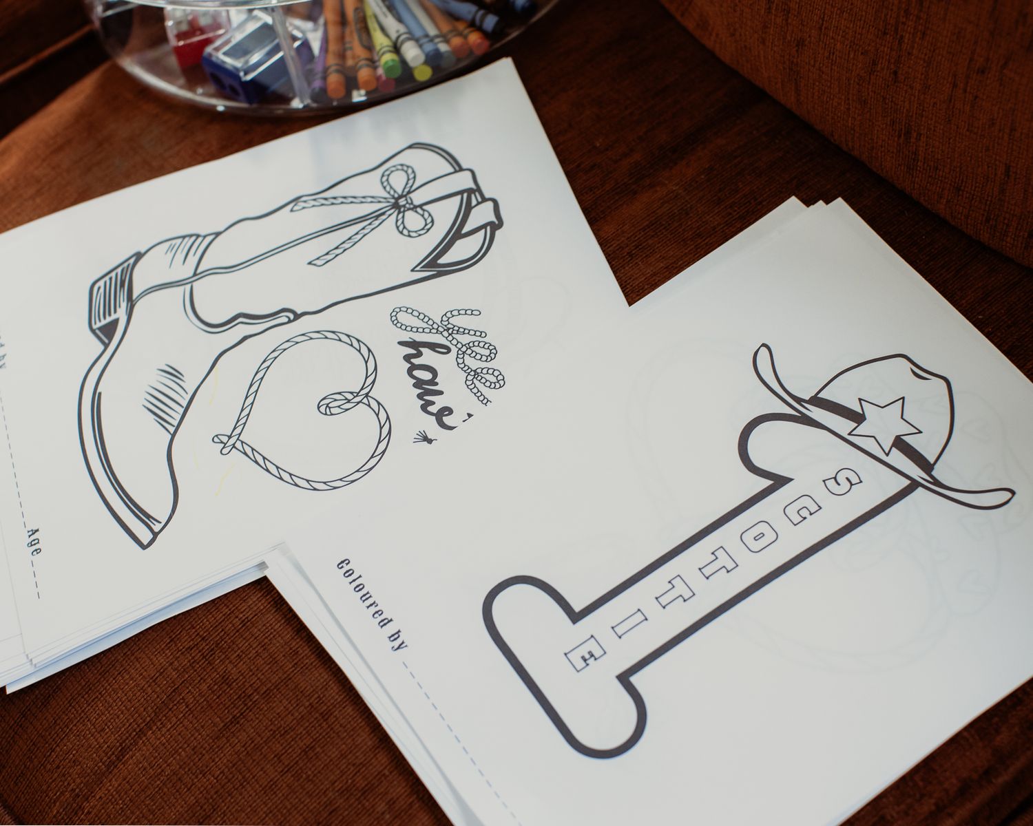 Cowboy boot and hat coloring pages laid out on a wooden table for a kids party.
