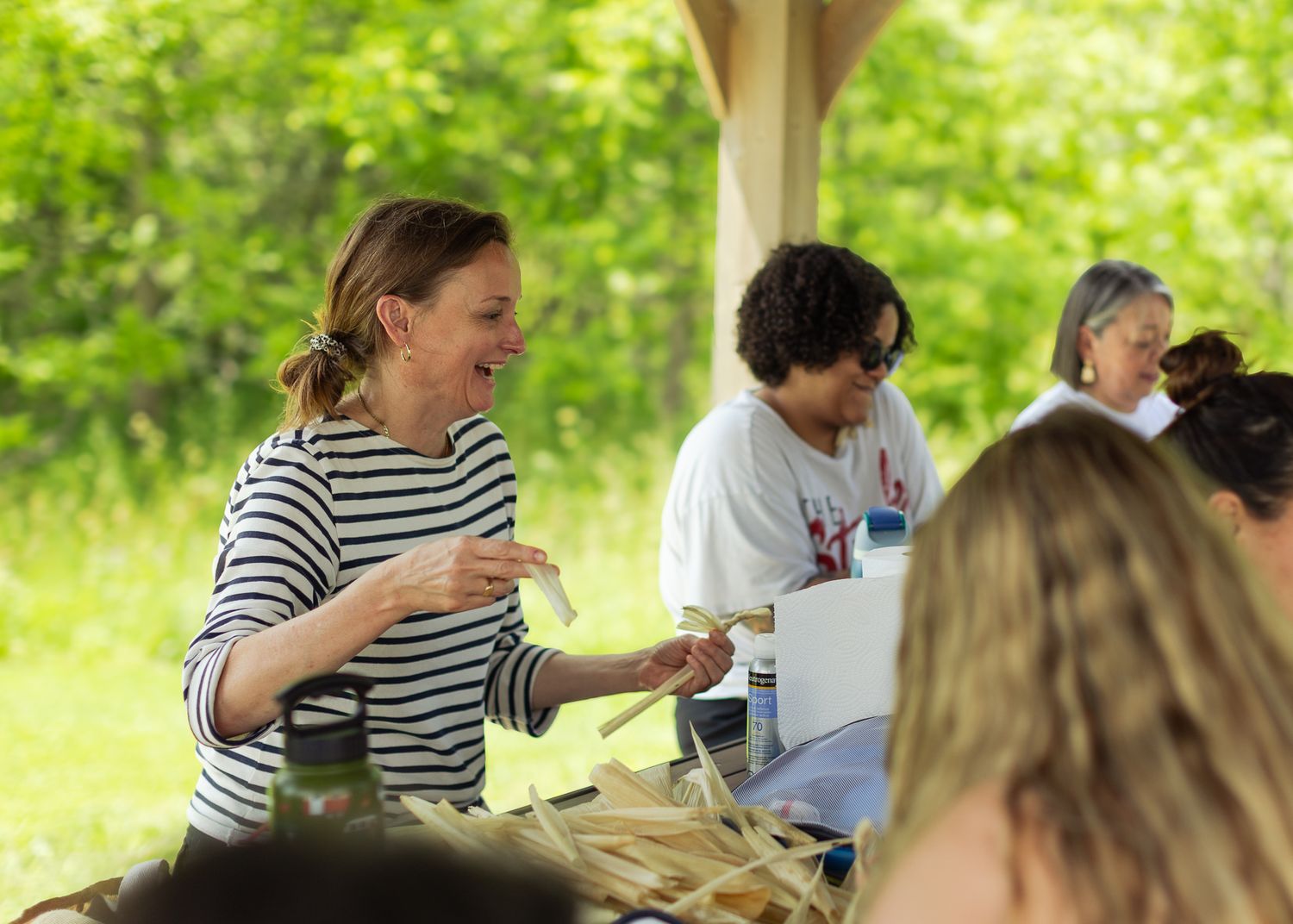 Woman in striped shirt serving food outdoors at a sunny community gathering.