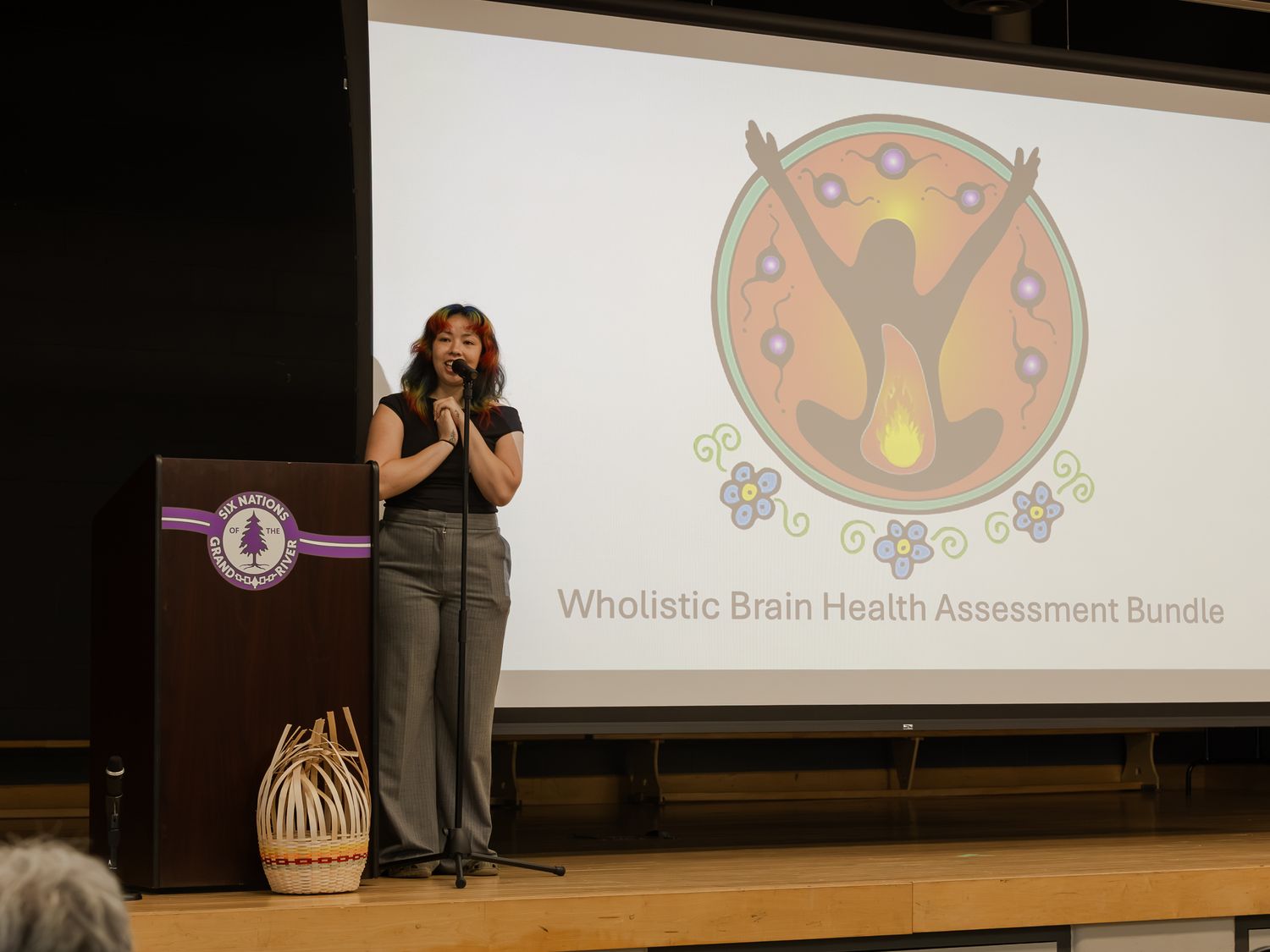 Woman presenting Wholistic Brain Health Assessment Bundle at a podium on stage.