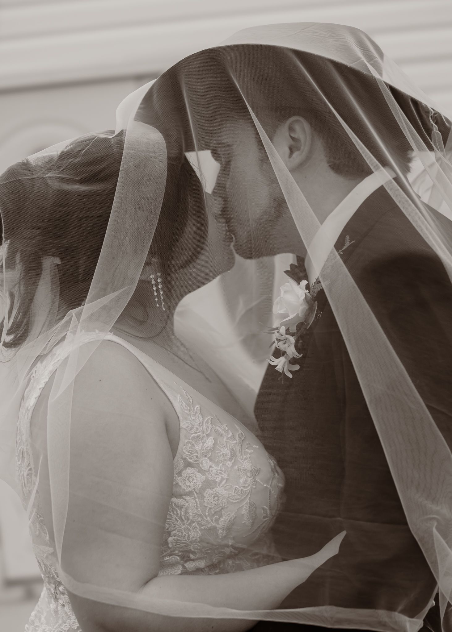 Black and white photo of bride and groom kissing under wedding veil.