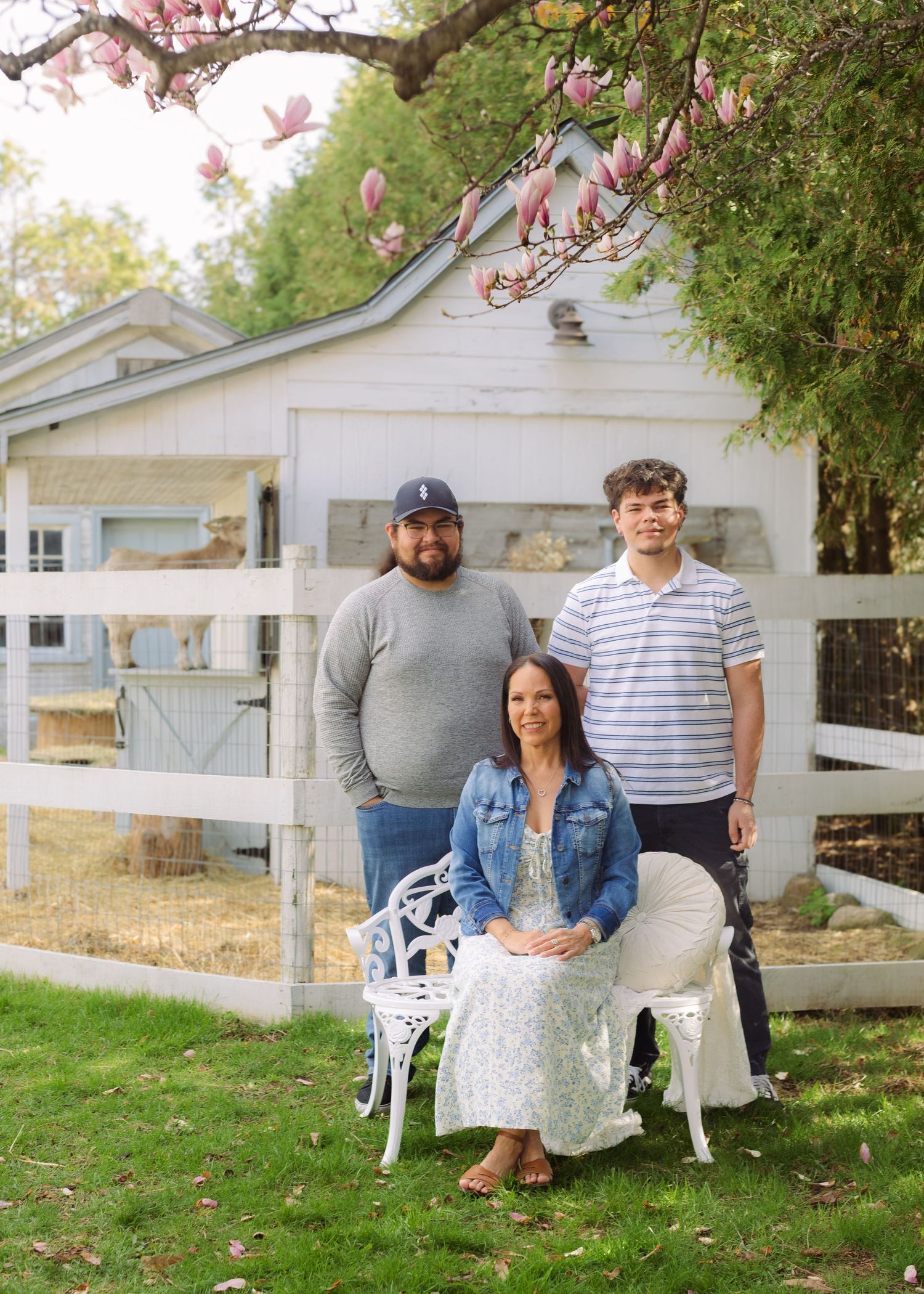 Family portrait of a woman seated and two young men standing behind her in a garden with a white fence.