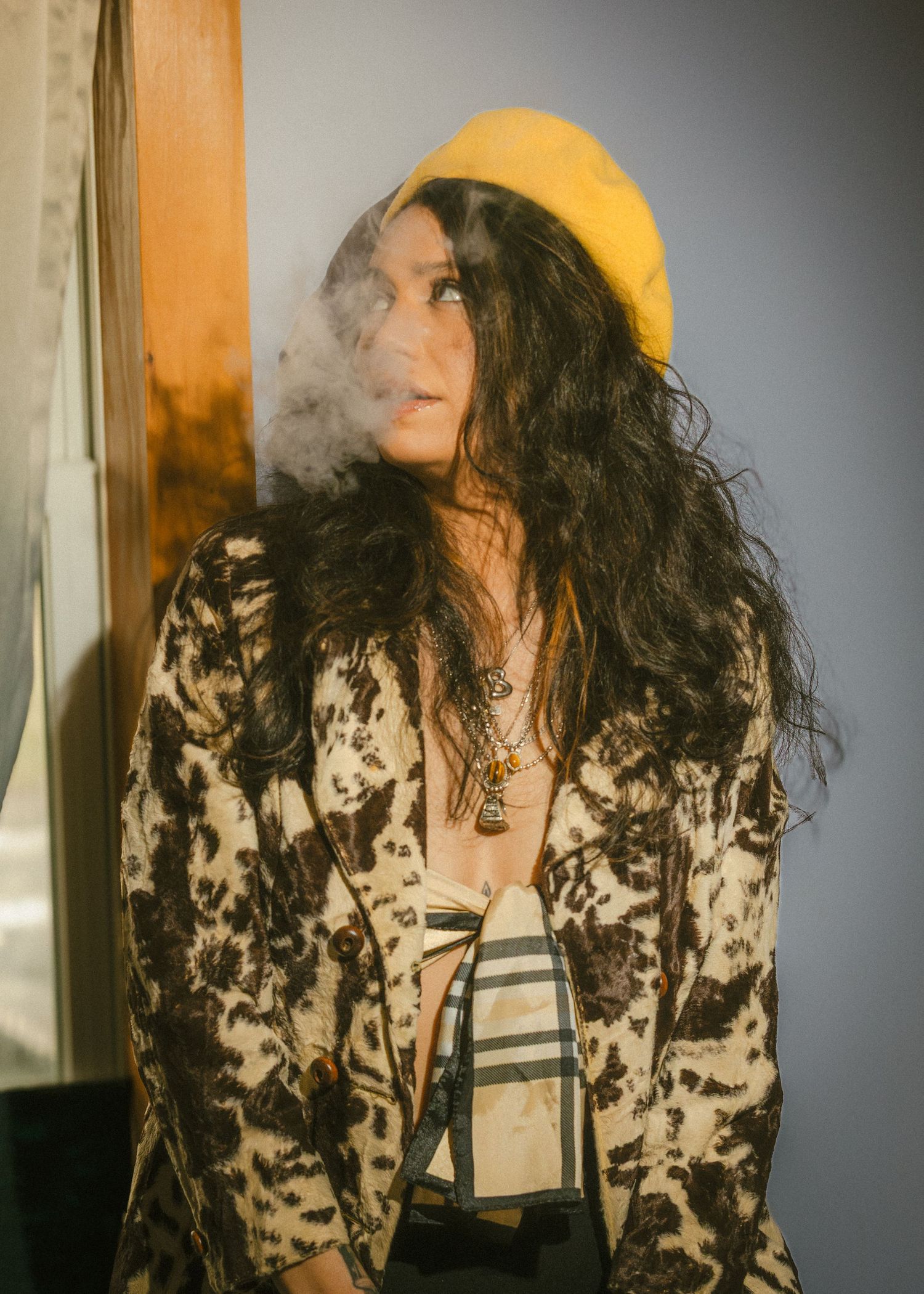 Woman in floral jacket and yellow beret exhaling smoke indoors in artistic portrait.