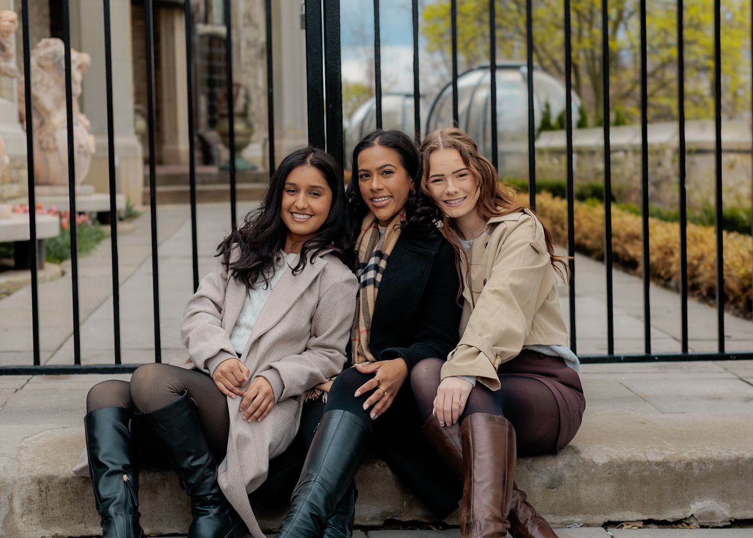 Three women posing together by an iron gate outdoors.