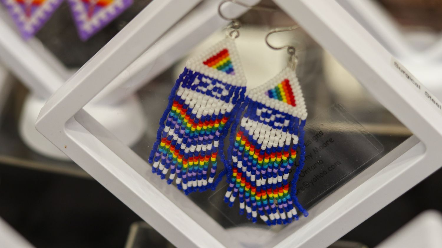 Handmade beaded earrings with rainbow and geometric patterns in blue, white, and multicolor Native American style.