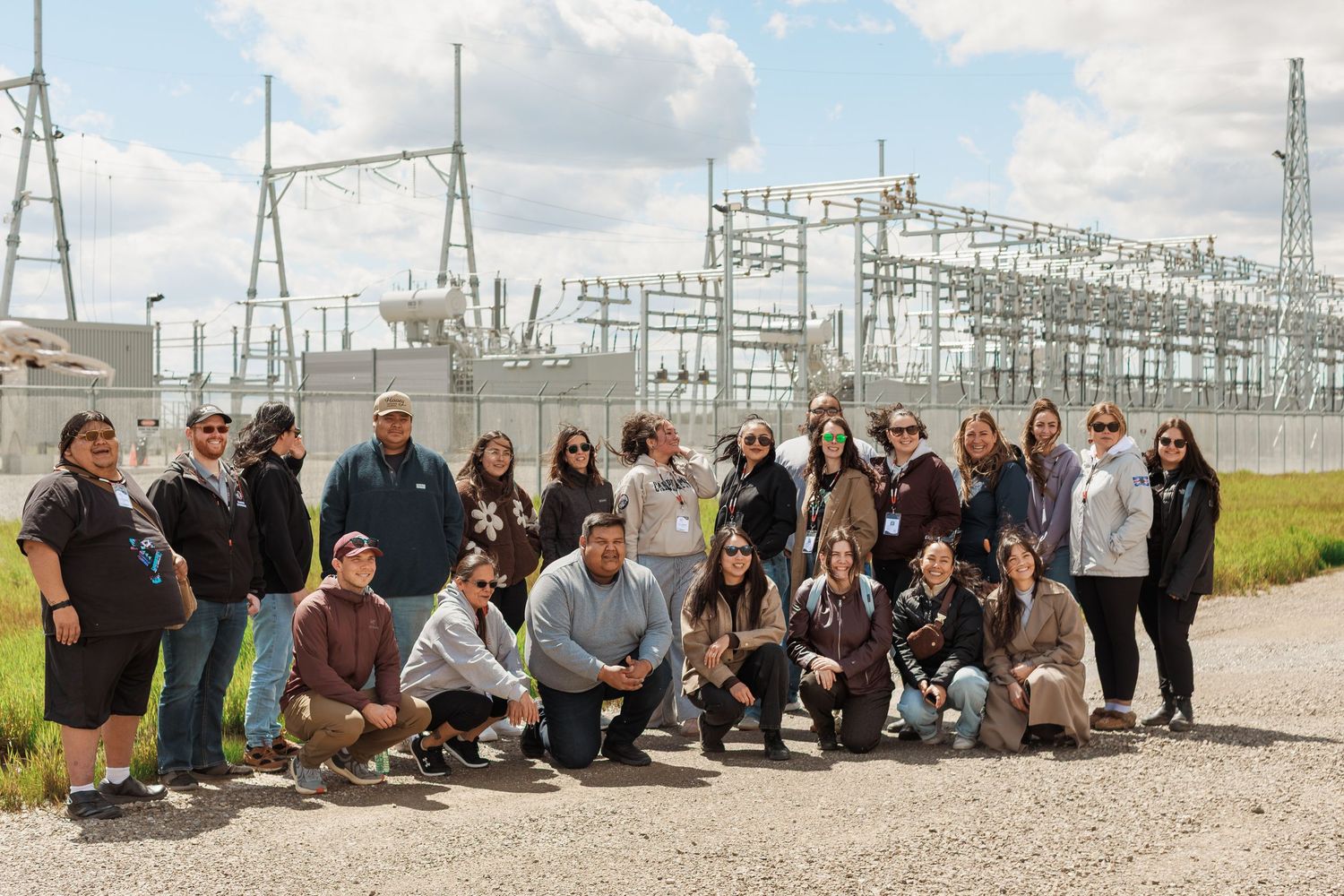Group of people posing outdoors near an electrical substation on a cloudy day.