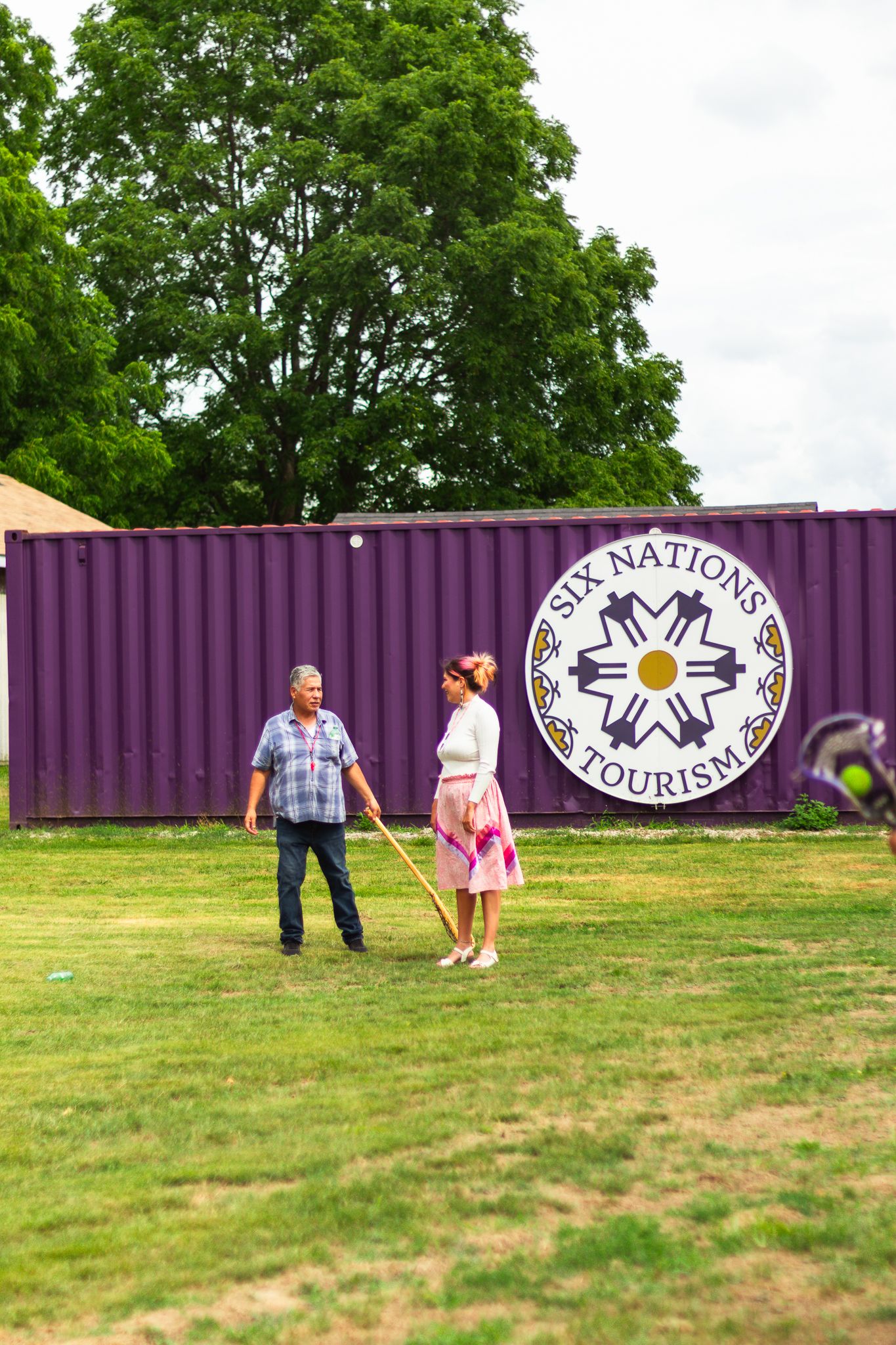 People playing outdoor games near a purple tourism banner on a grassy field.