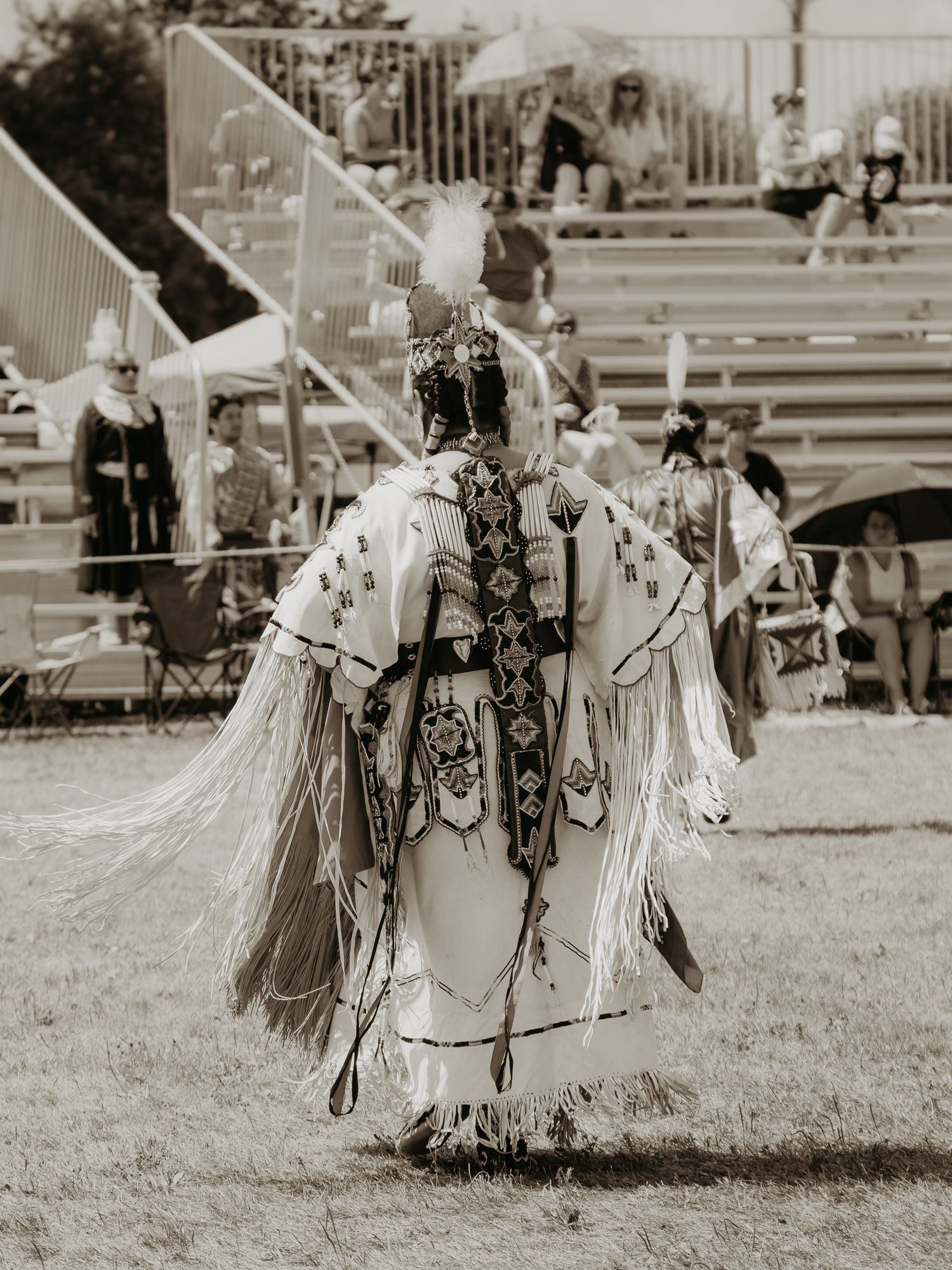 A powwow dancer in ornate white regalia with intricate beadwork performing at an outdoor venue.