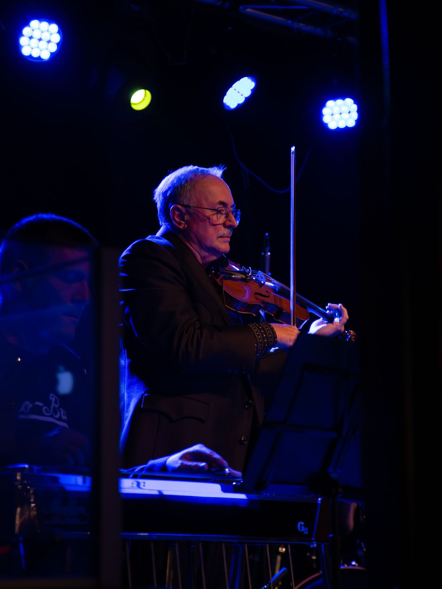 A violinist in formal attire performs under dramatic blue stage lighting.