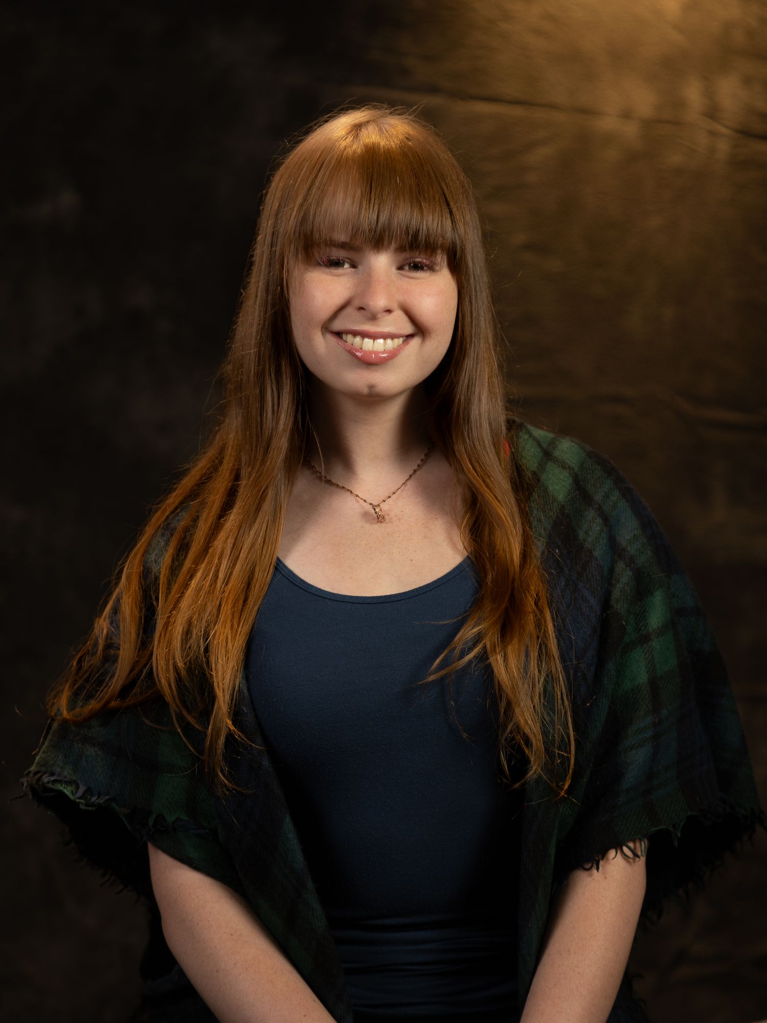 Studio portrait with dramatic lighting showing person in dark top with plaid wrap.