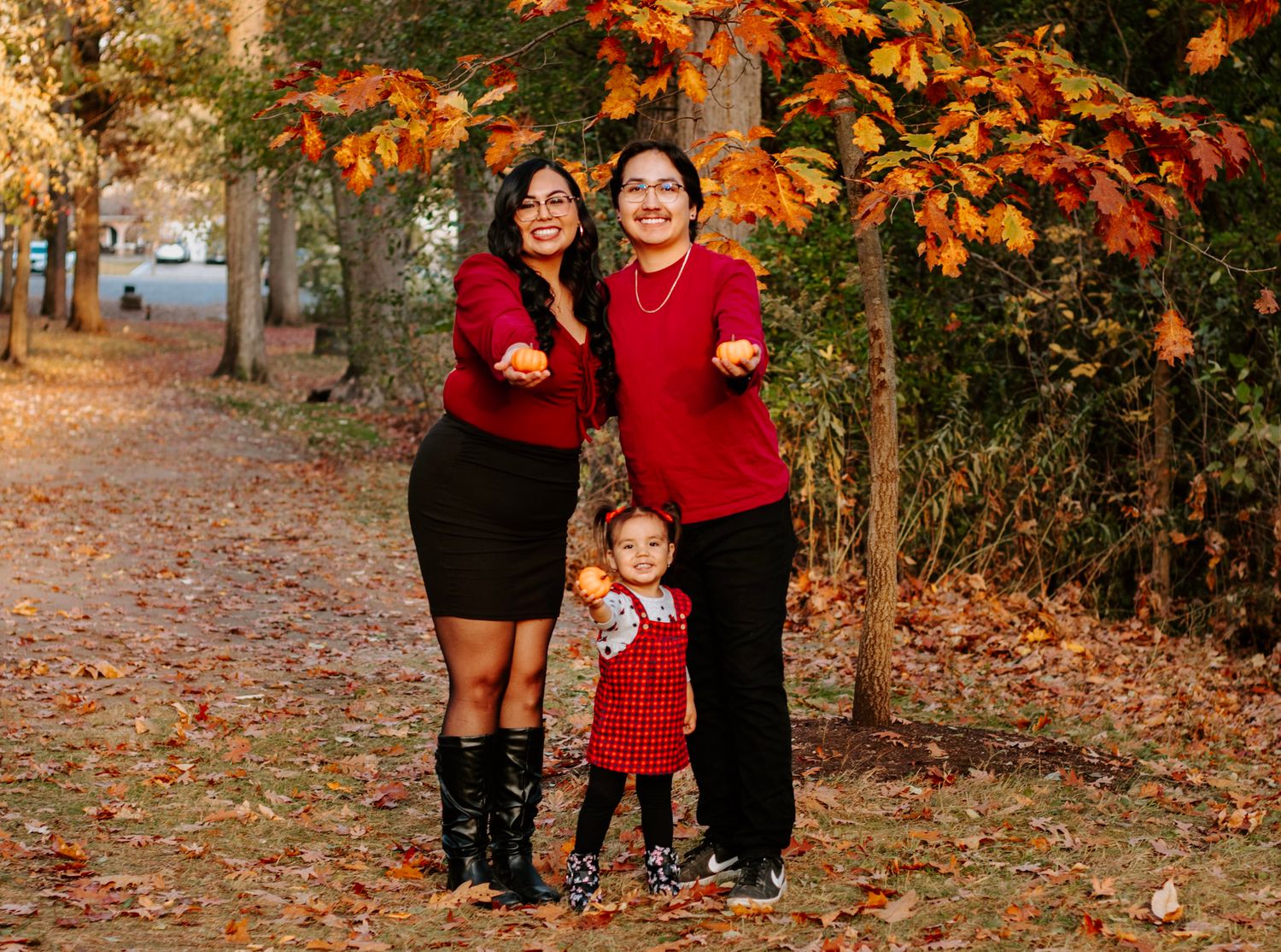 Family portrait in matching red outfits surrounded by vibrant fall leaves and trees.
