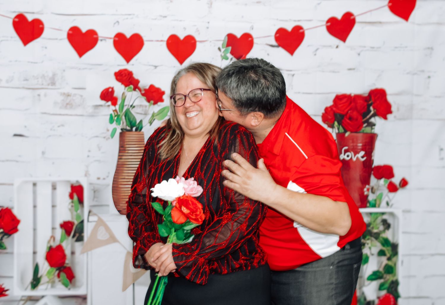 Valentine's Day photo session with red hearts and roses against white brick backdrop.