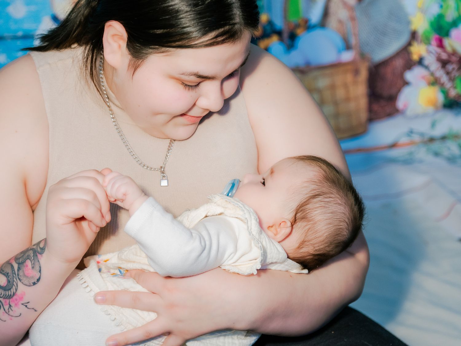 A young mother with tattoos tenderly gazes at her newborn baby while bottle feeding indoors.