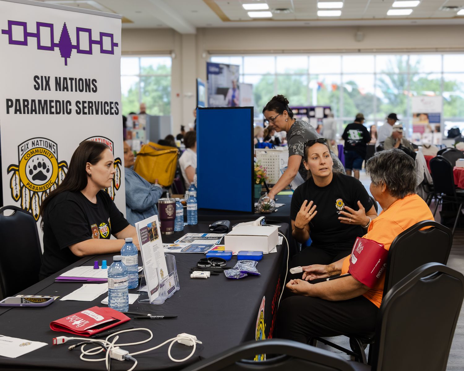 Six Nations Paramedic Services staff engage with a visitor at an indoor health and wellness expo booth.