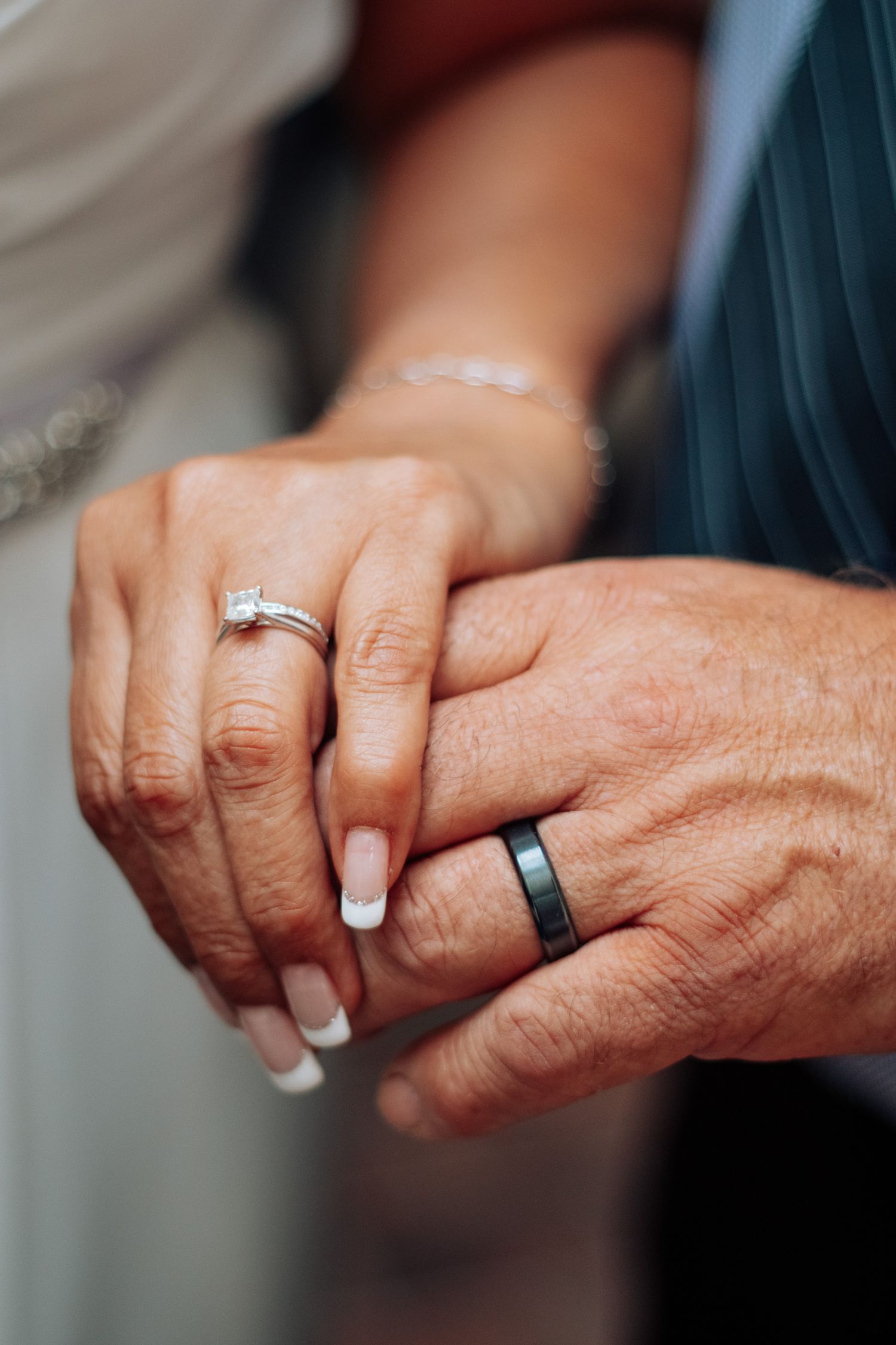 Close-up of newlywed couple holding hands, bride wearing diamond engagement ring and groom wearing black wedding band.