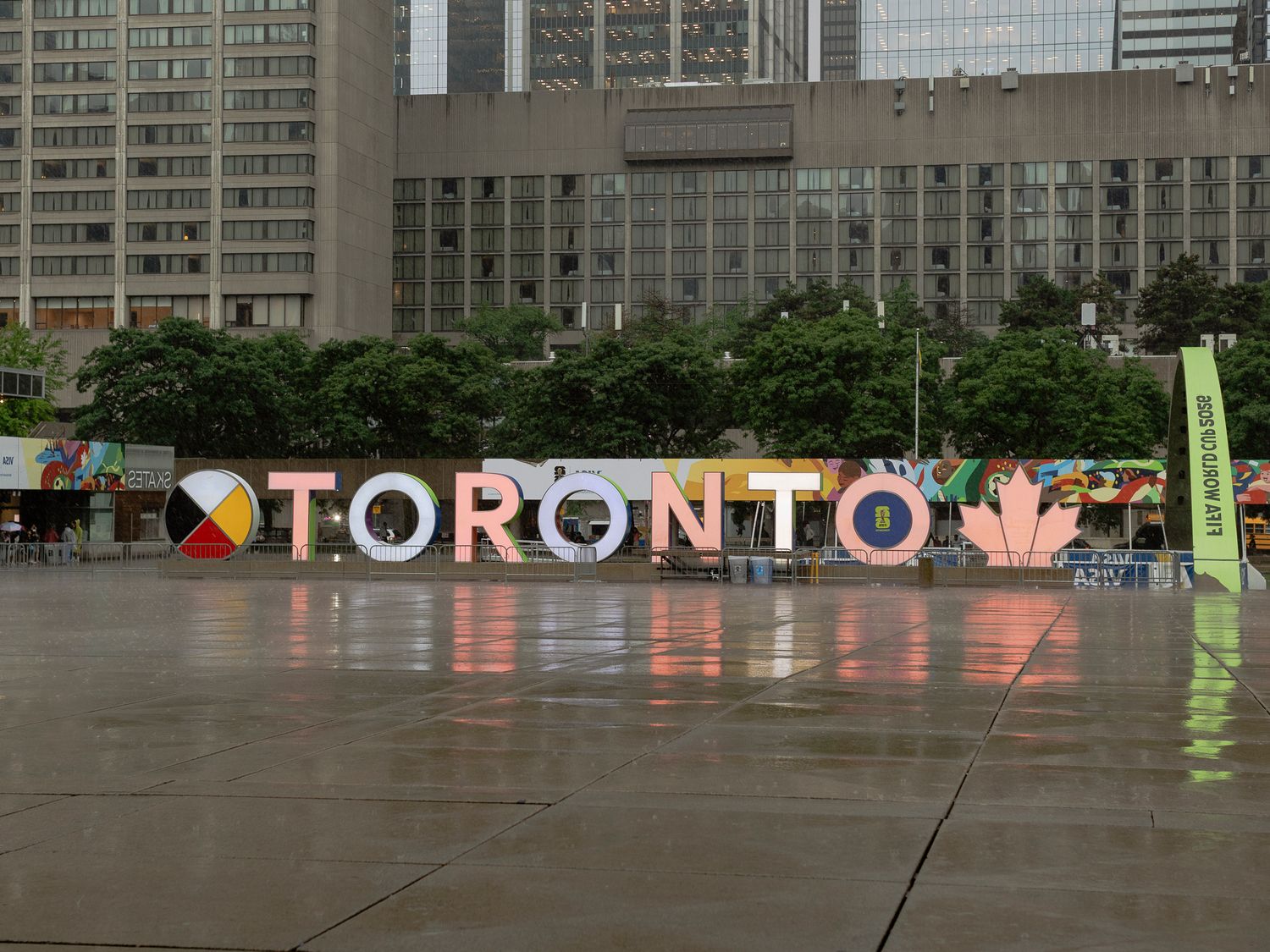 Colorful Toronto sign installation at Nathan Phillips Square on a rainy day with city buildings in background.