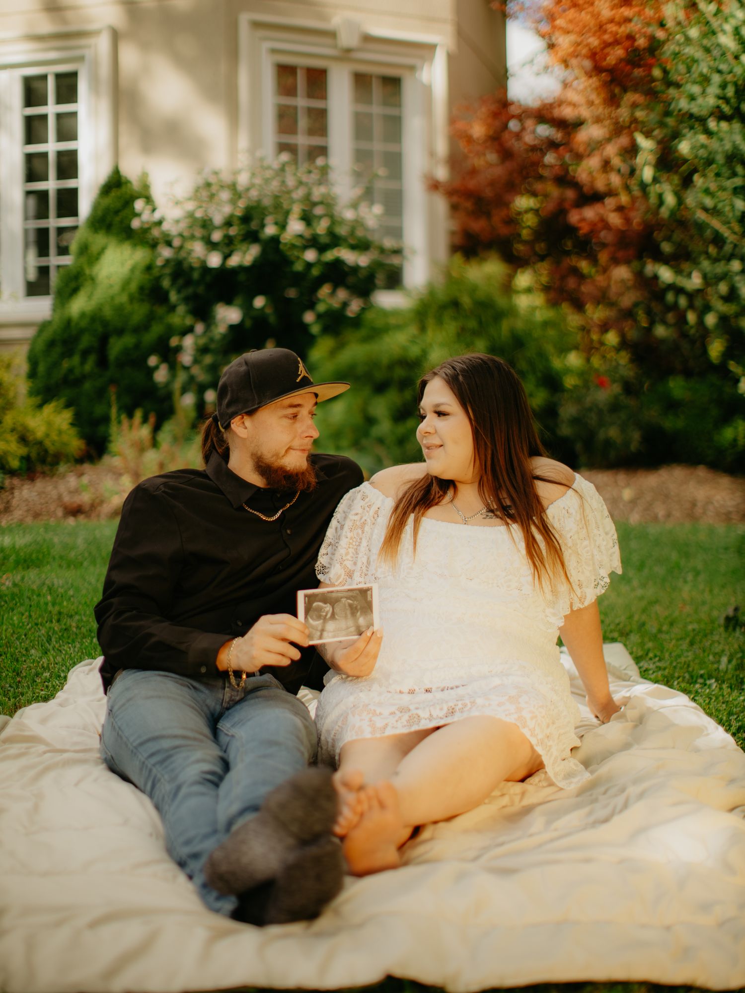 A couple sits on a blanket in a garden sharing a tender moment during an autumn photoshoot.