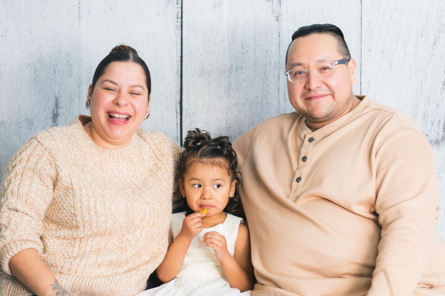 Family photo series with parents and young child against white backdrop.