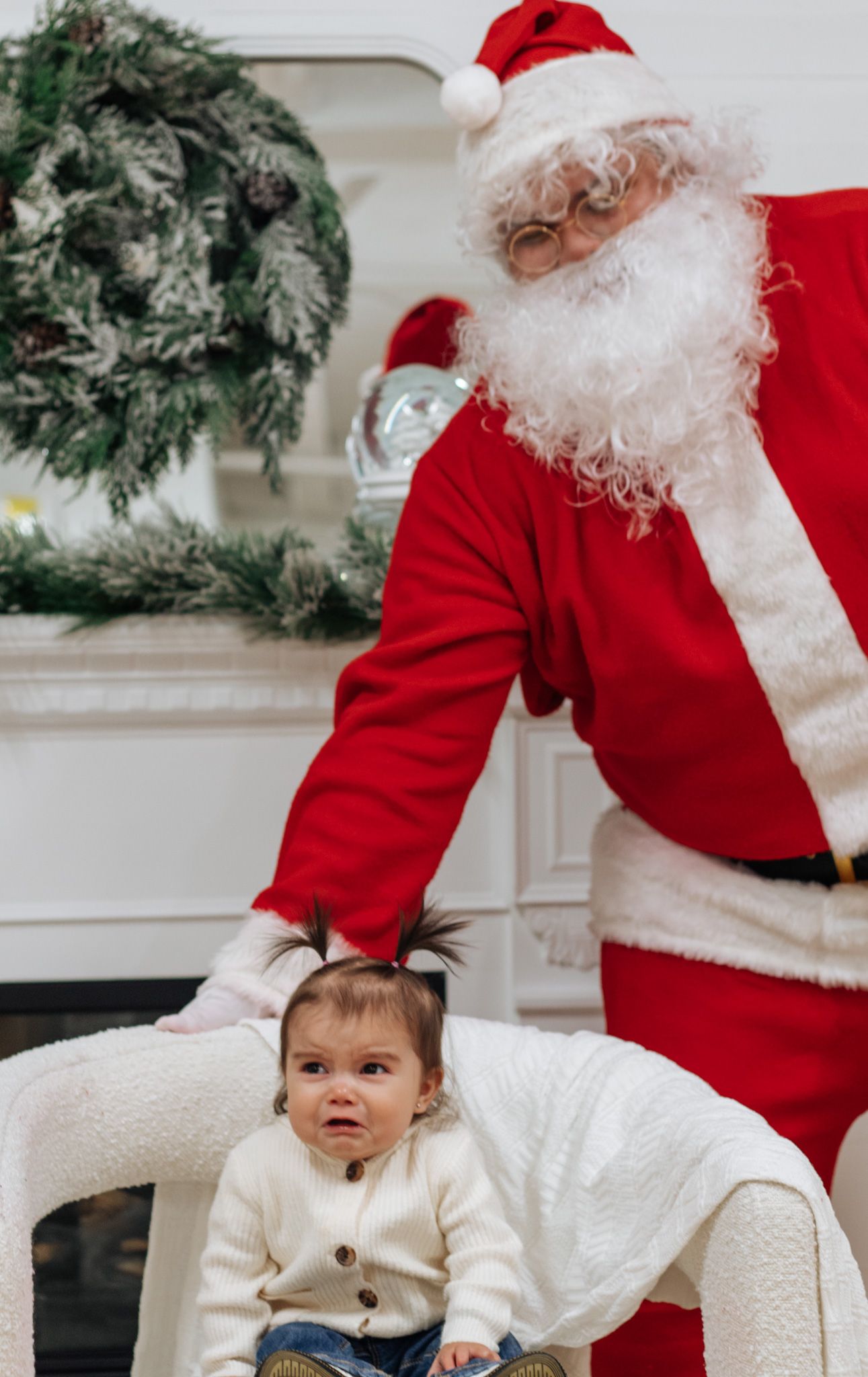 Santa Claus interacting with child in front of decorated white Christmas trees during photo session.