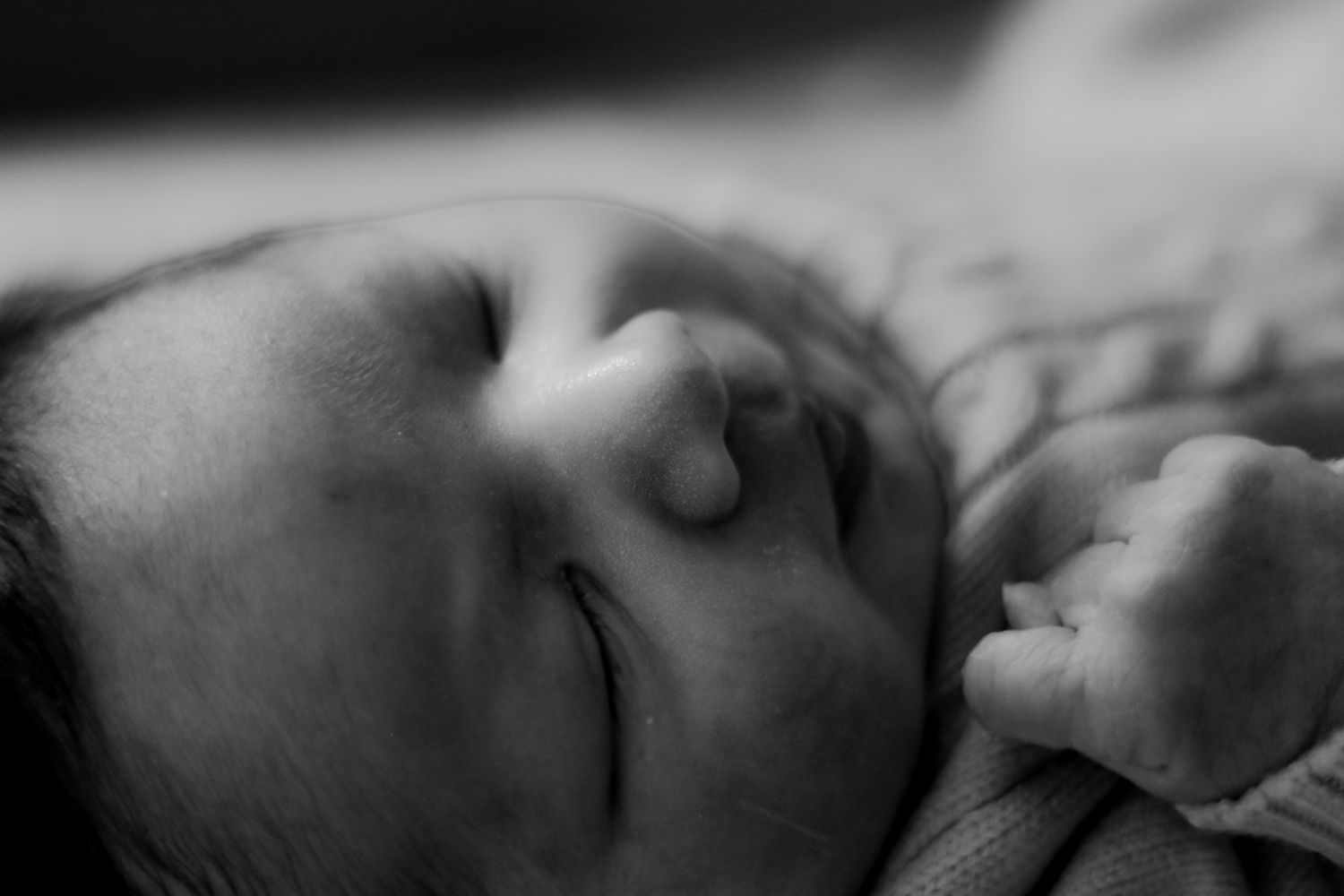 Side view of infant sleeping peacefully against white fabric in black and white.