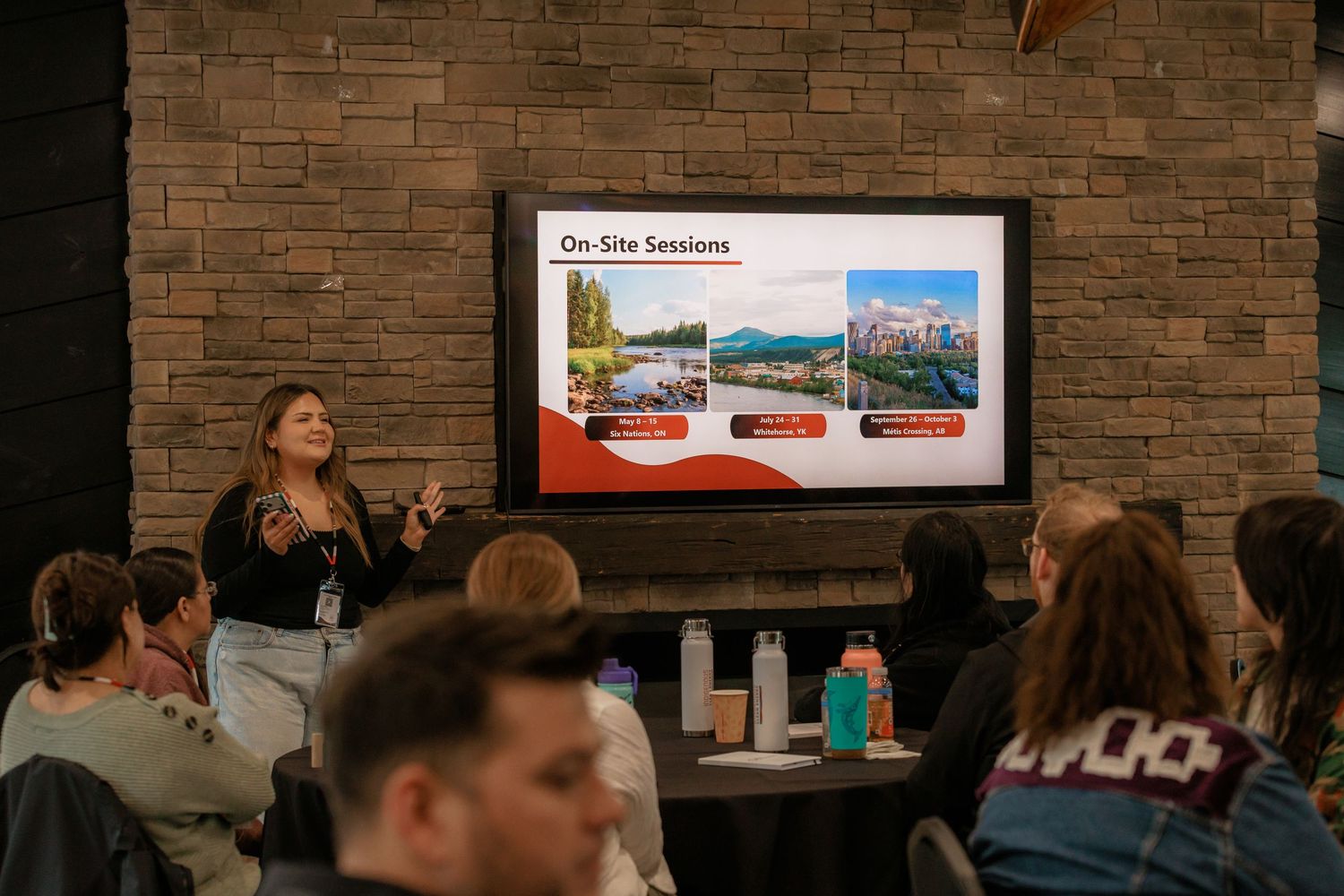 Woman presenting On-Site Sessions on a large screen to an engaged audience in a modern conference room.