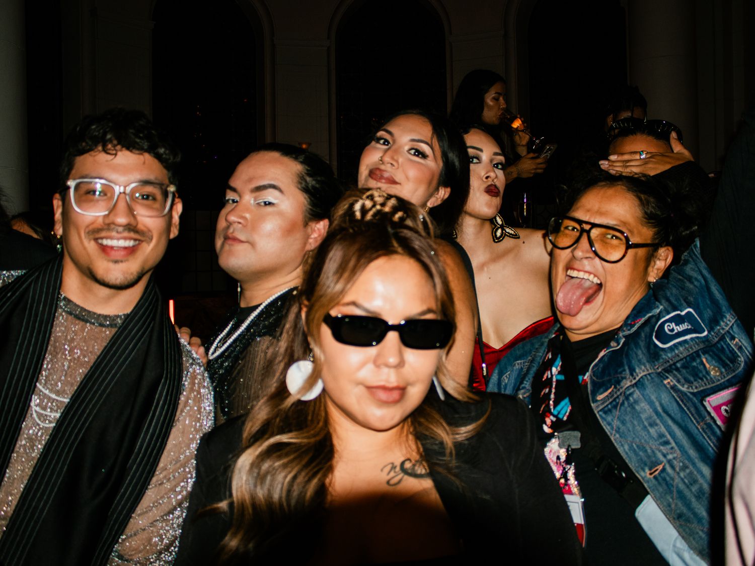 Group of six friends smiling and posing together at an indoor nighttime party event.