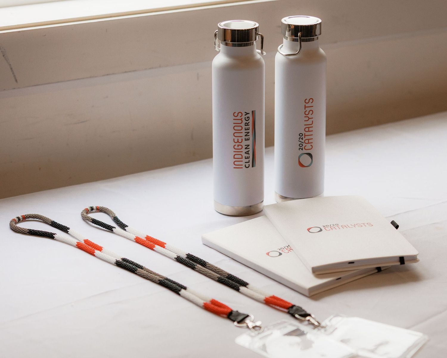 Conference branded merchandise including two white water bottles, lanyards, notebooks, and name badges on a table.