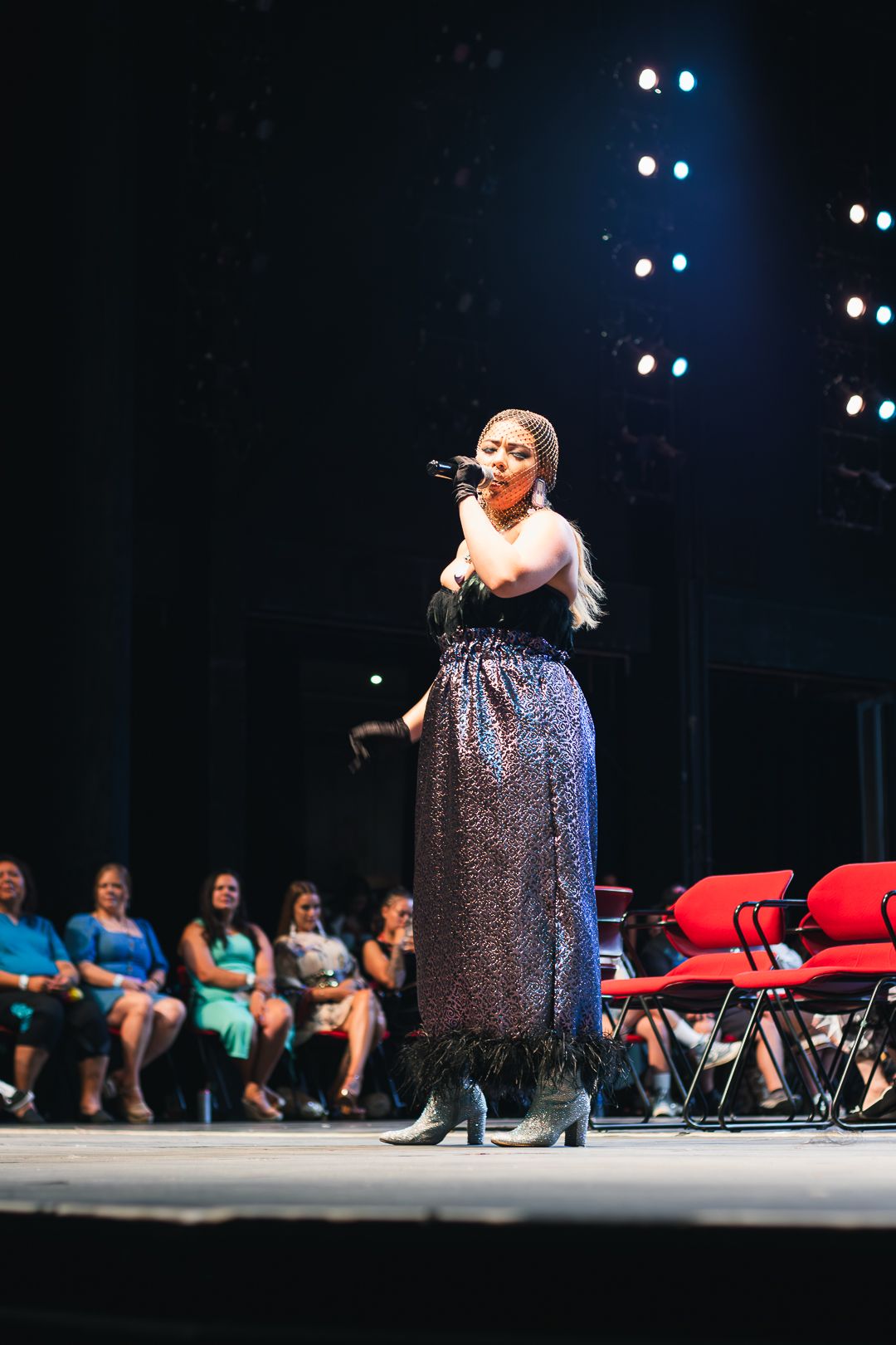 Performer in glittery cape on stage with dramatic spotlighting.