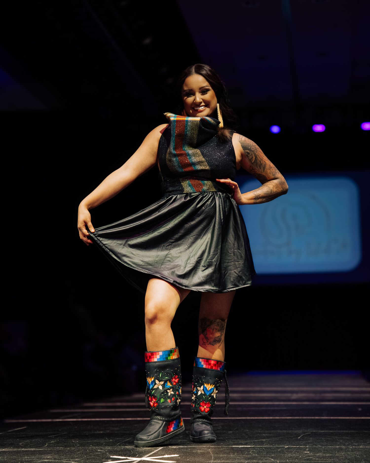 Dancer performing in black dress and colorful patterned boots on stage.