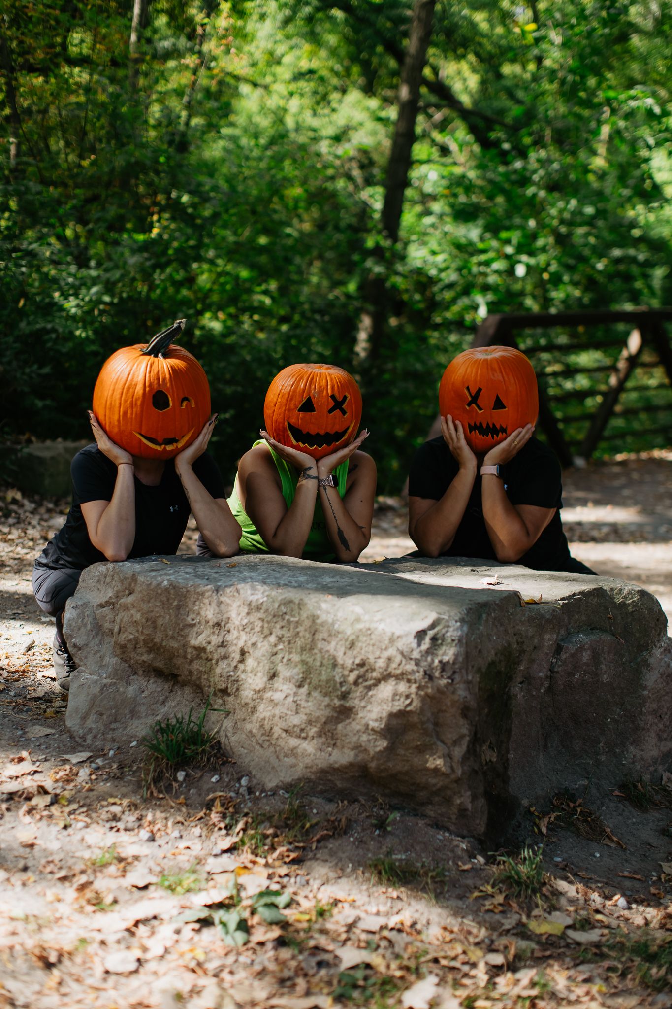 Three carved jack-o'-lanterns arranged on a stone wall in a wooded setting.