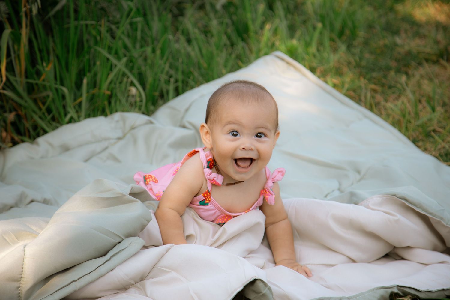 Baby photoshoot on a white blanket outdoors in natural lighting.