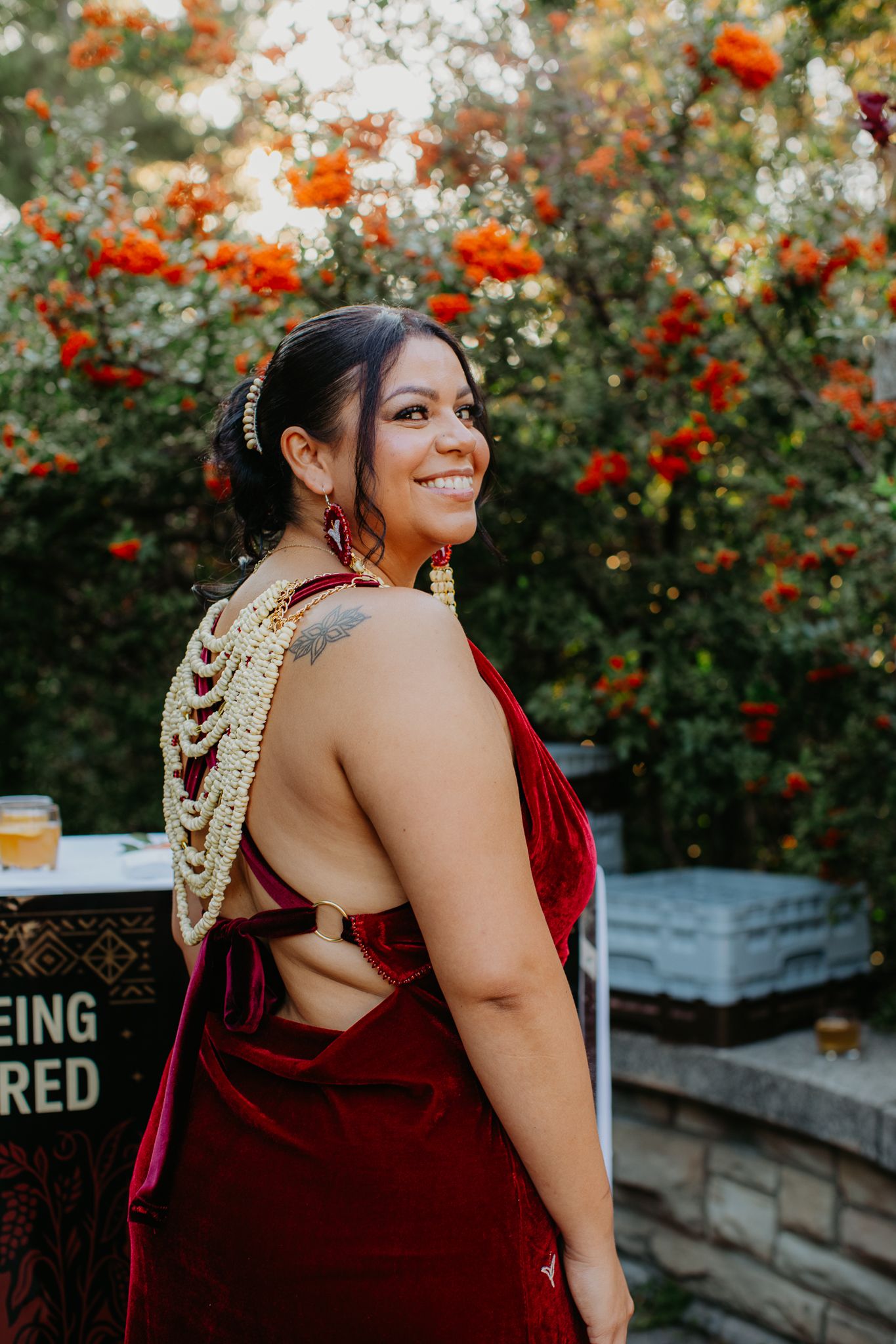 Woman in backless red velvet gown with gold floral jewelry smiles at outdoor Seeing Red event.