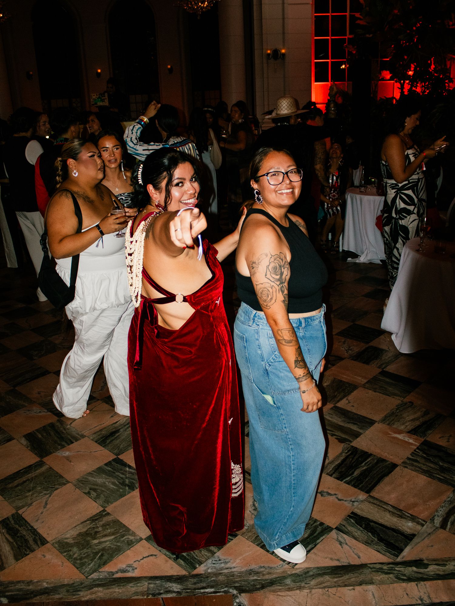 Two women dancing and posing at an indoor party with red ambient lighting in the background.