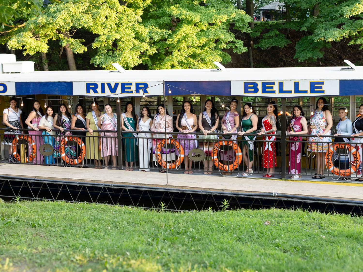 Miss Indigenous Canada pageant contestants pose on the River Belle boat deck in elegant attire.