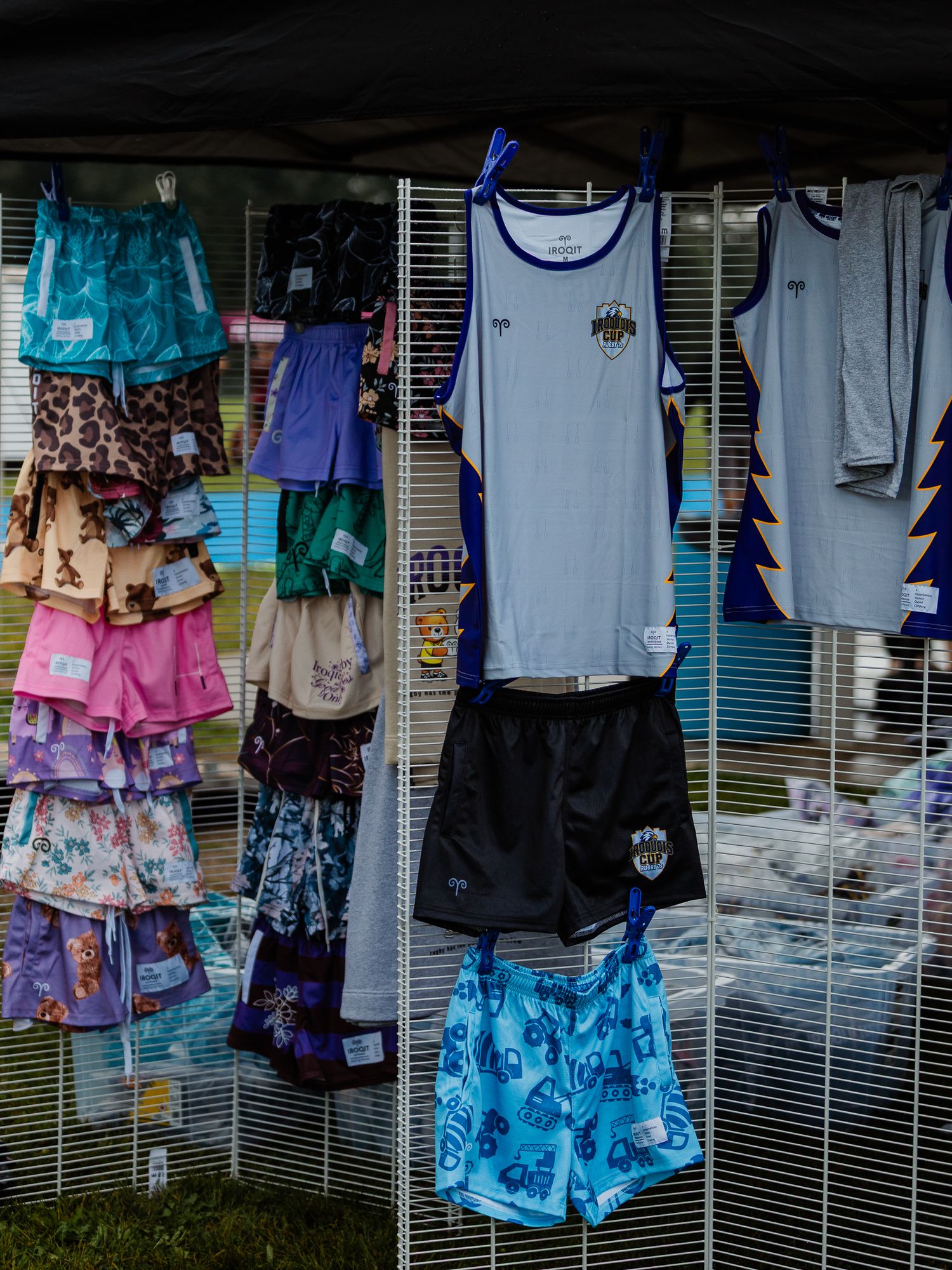 Colorful athletic shorts and tank tops displayed on a rack at an outdoor sports merchandise vendor booth.