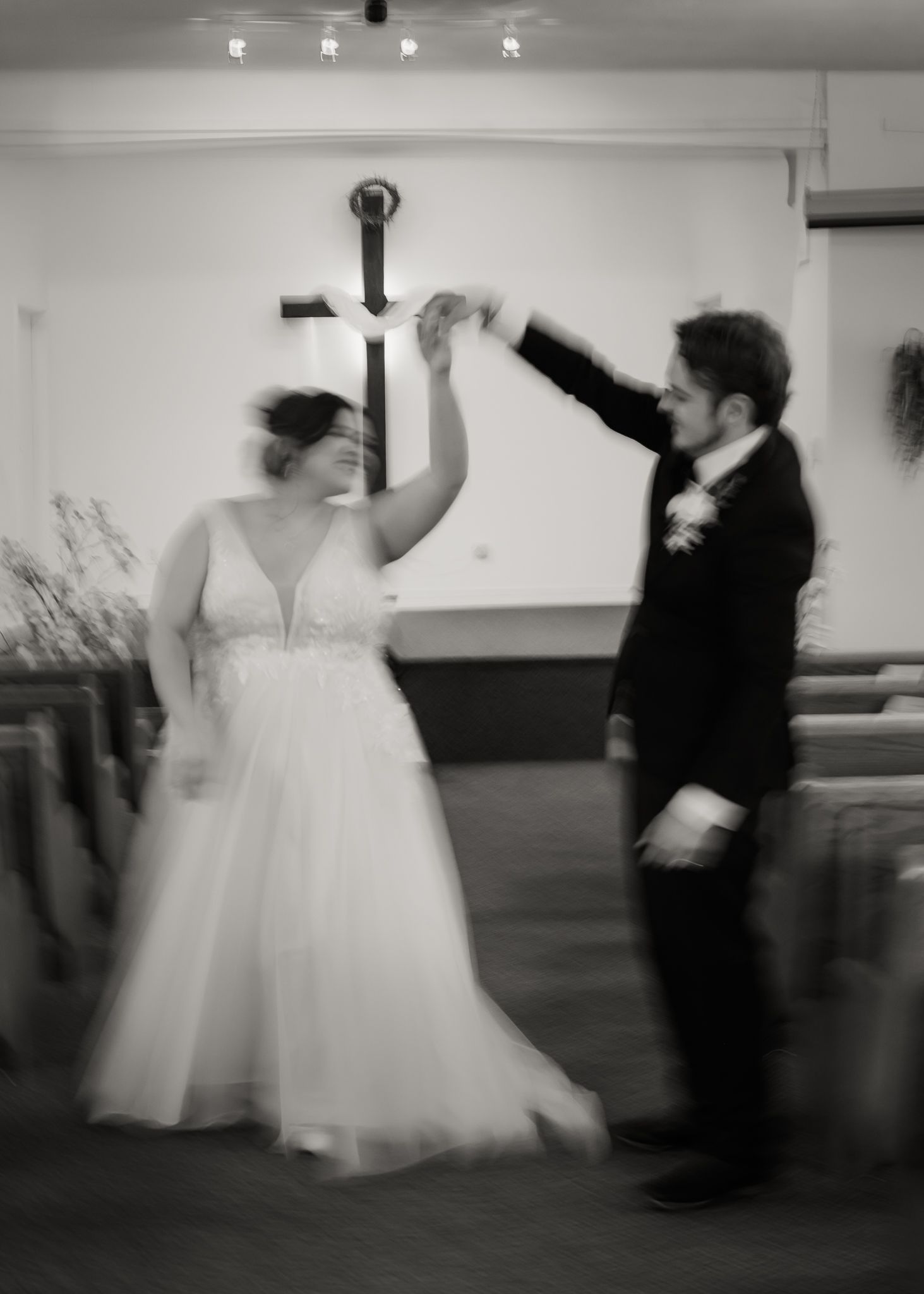 Black and white photo of bride and groom dancing in front of a church cross.