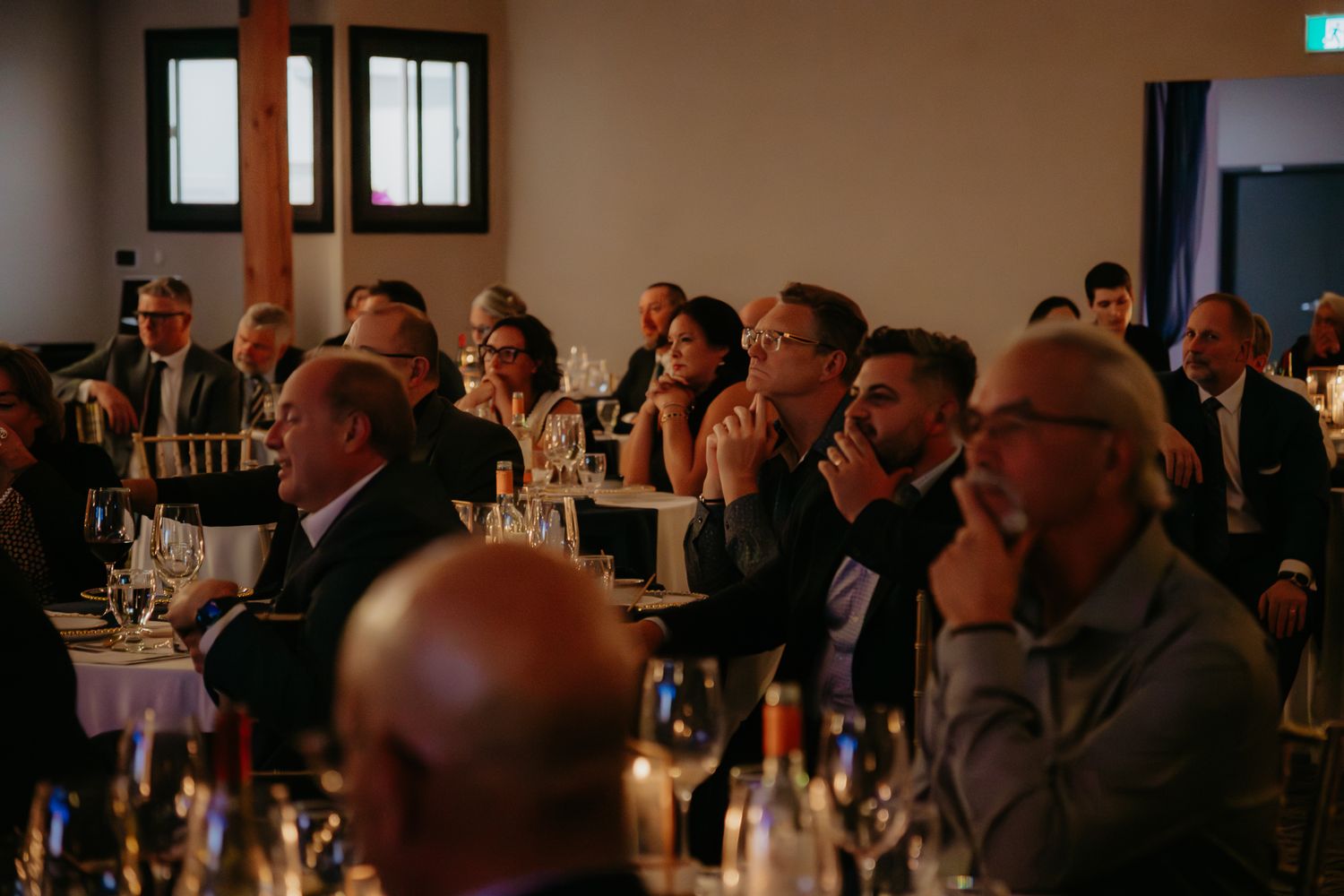 Event attendees gathered in a dimly lit room with tables and chairs during a formal celebration.