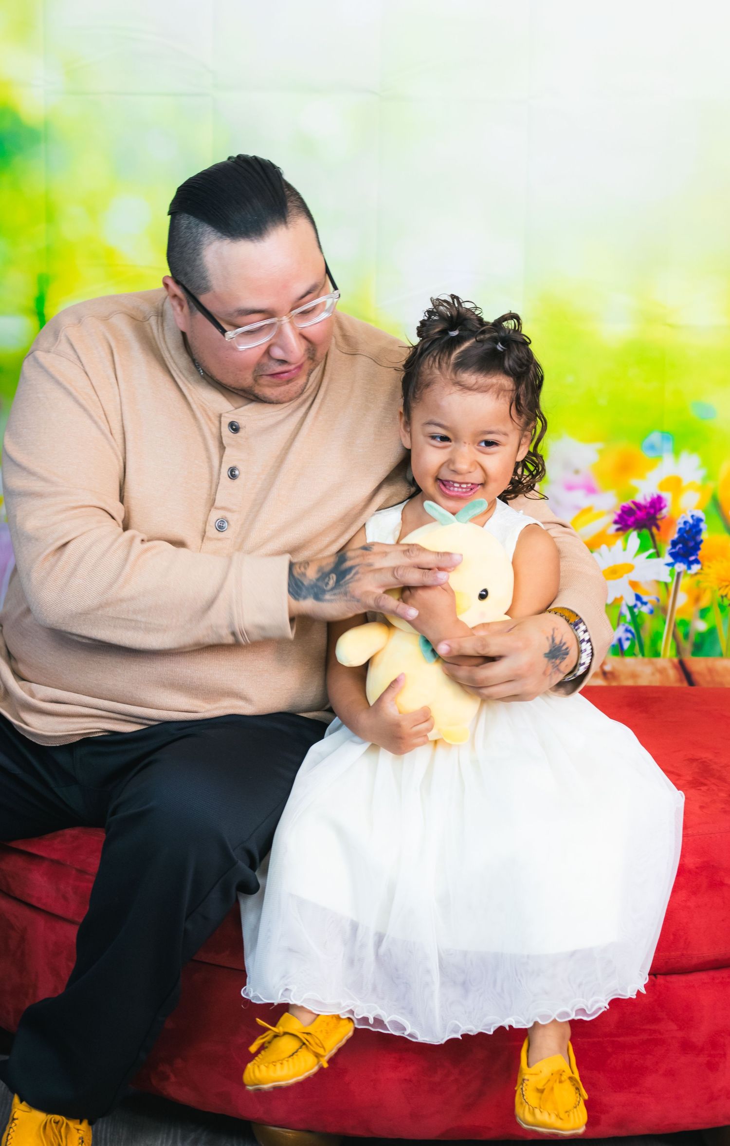 A heartwarming moment captured on a red velvet couch with bright floral background.