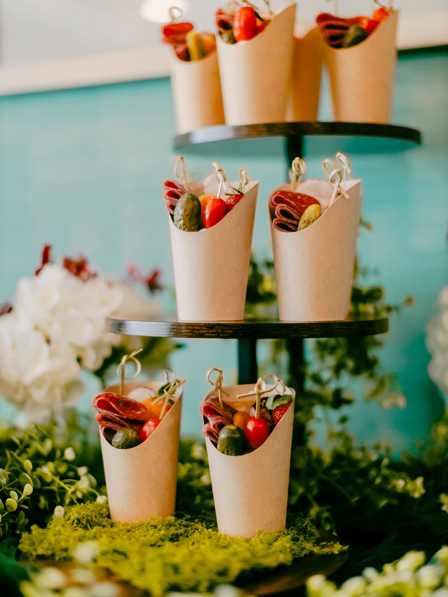 Elegant tiered display stand with kraft paper cones filled with fresh vegetables and charcuterie at a catered event.
