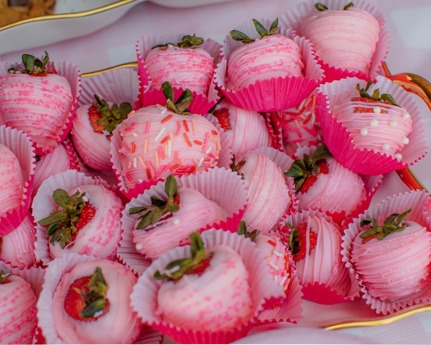 Pink chocolate-dipped strawberries in pink cupcake liners arranged on a decorative plate.