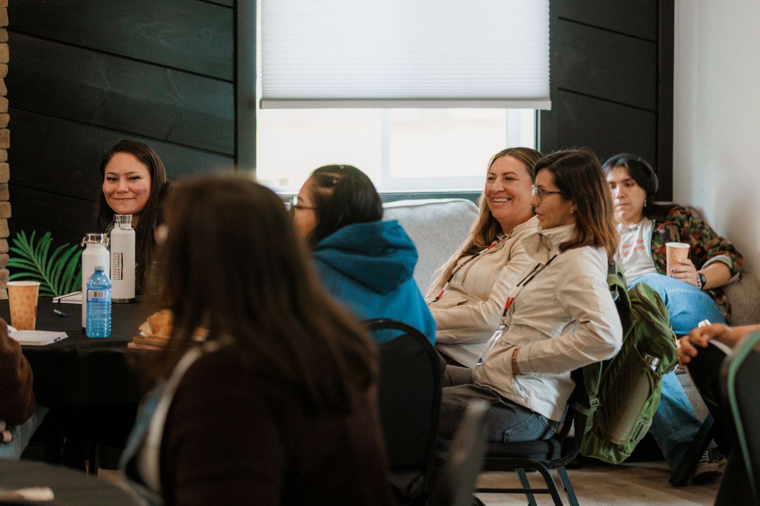 A group of women smile and engage during an indoor community meeting at a modern venue.