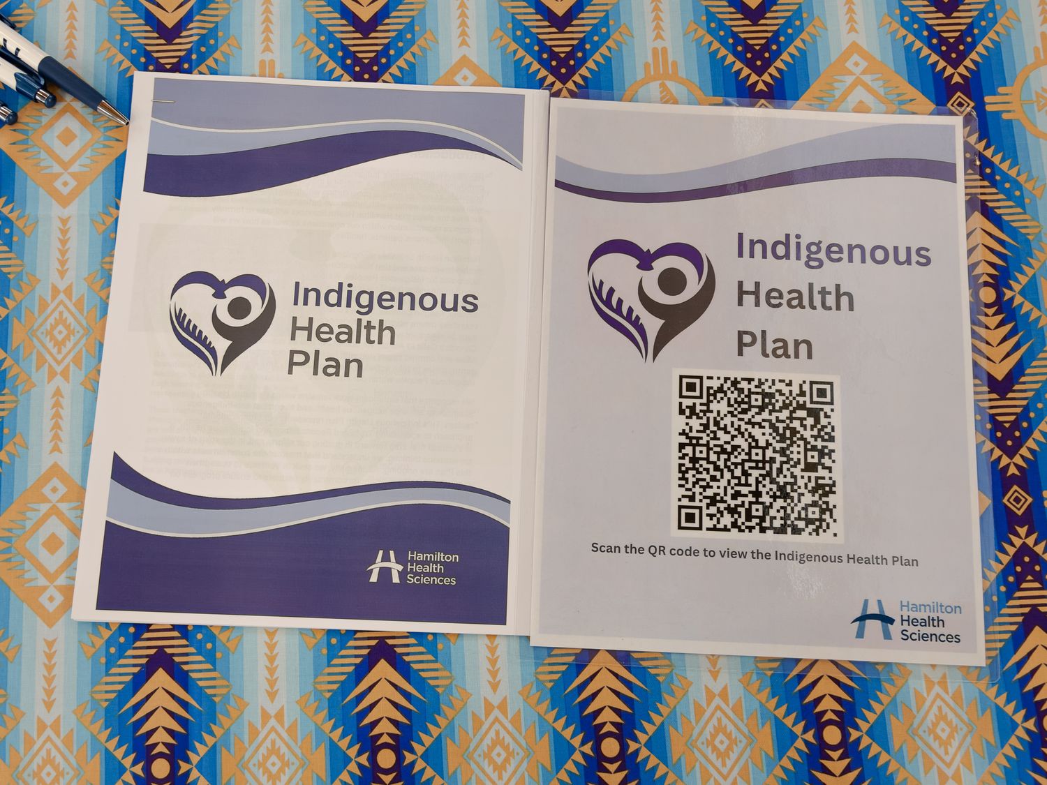 Two Indigenous Health Plan brochures with QR code displayed on a patterned Indigenous textile.