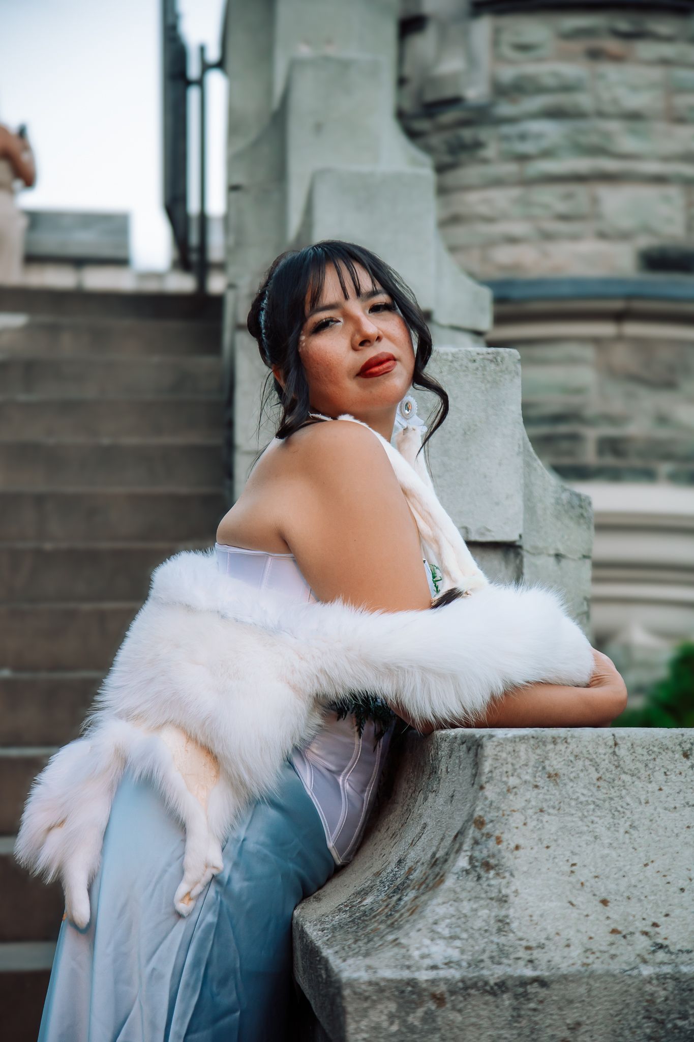 Person in white fur-trimmed dress posing against stone wall architecture.
