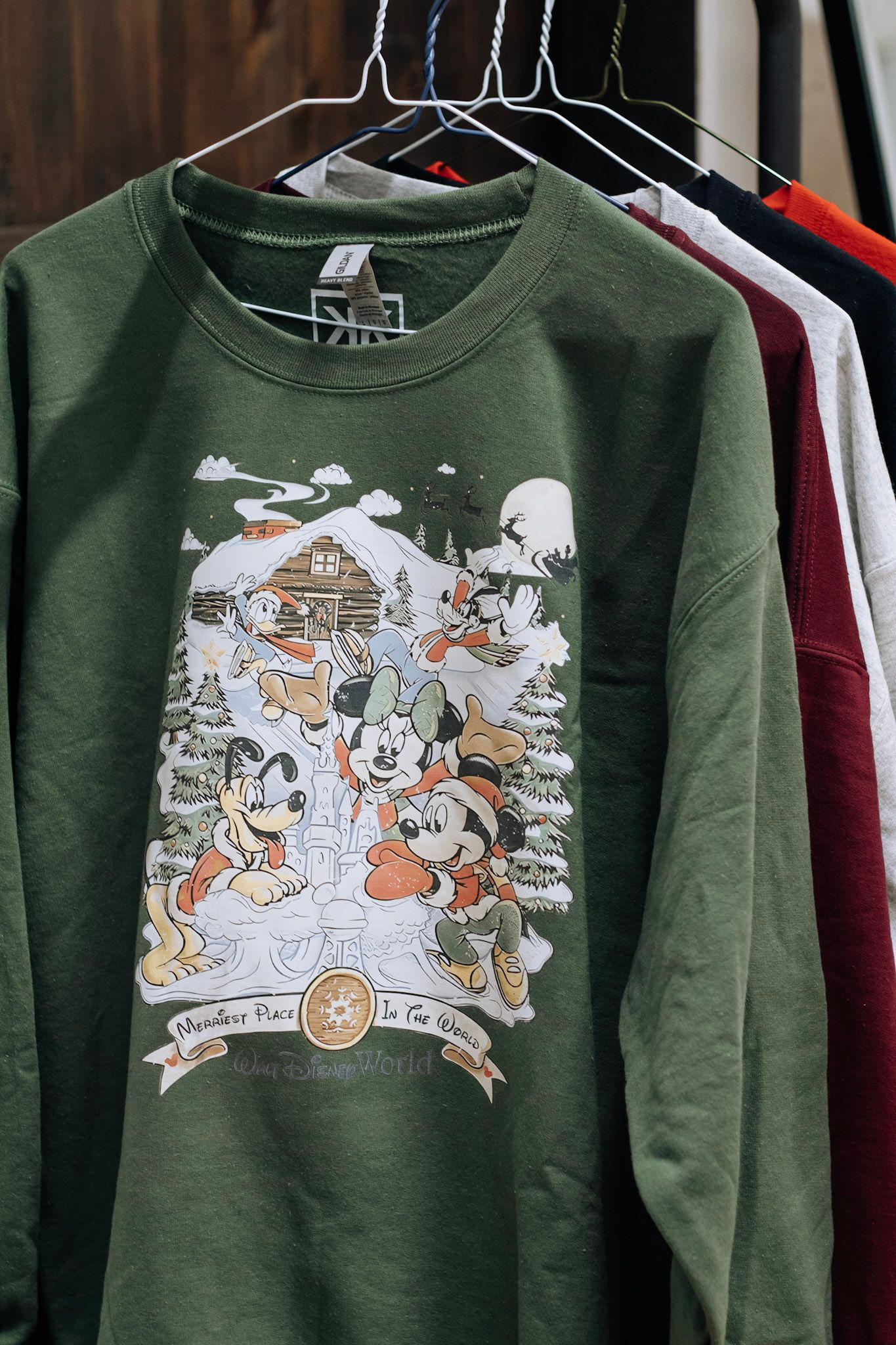 Collection of green holiday sweatshirts featuring Disney cartoon characters in winter scenes.