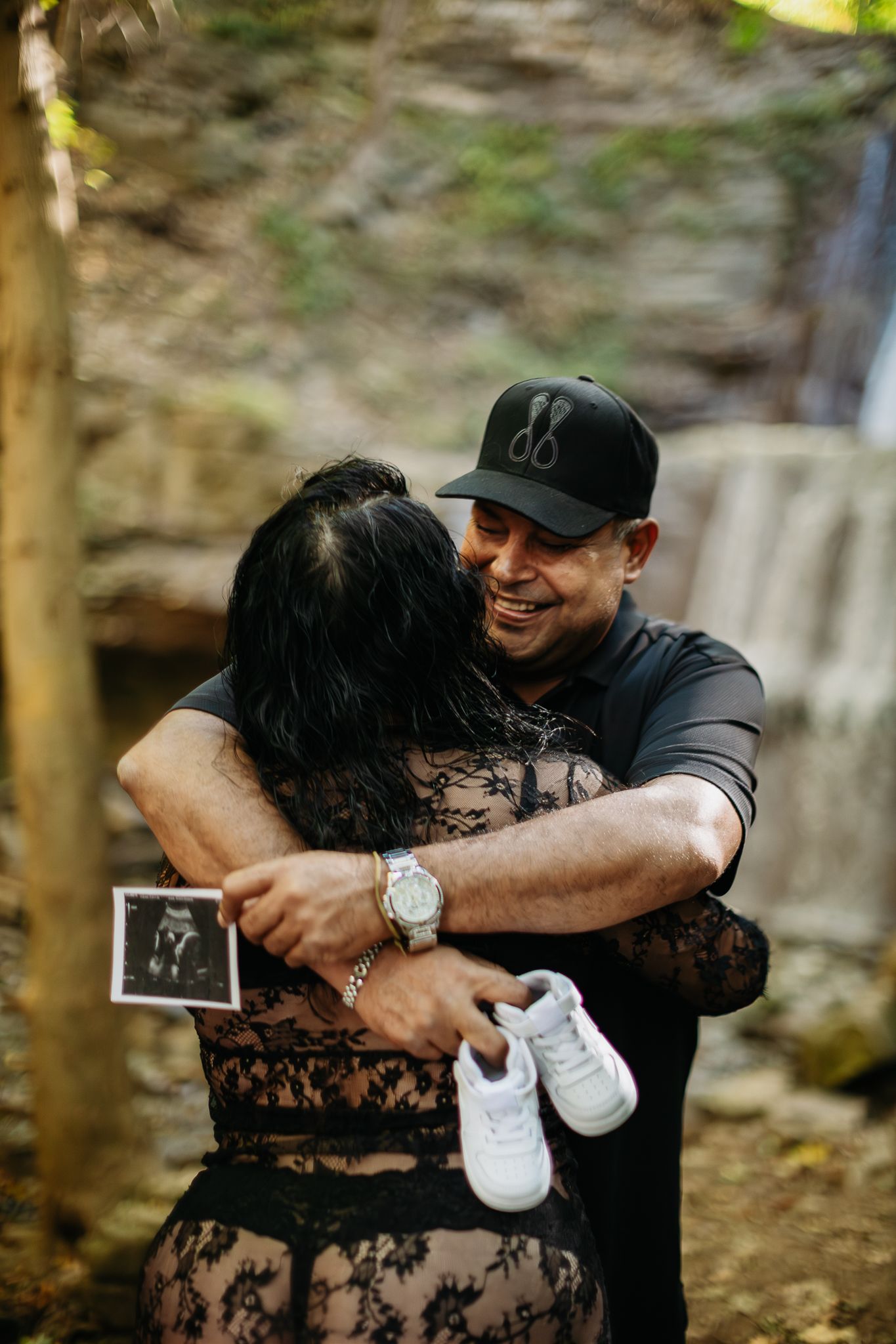 A couple embraces and laughs together during a romantic photoshoot by a waterfall.